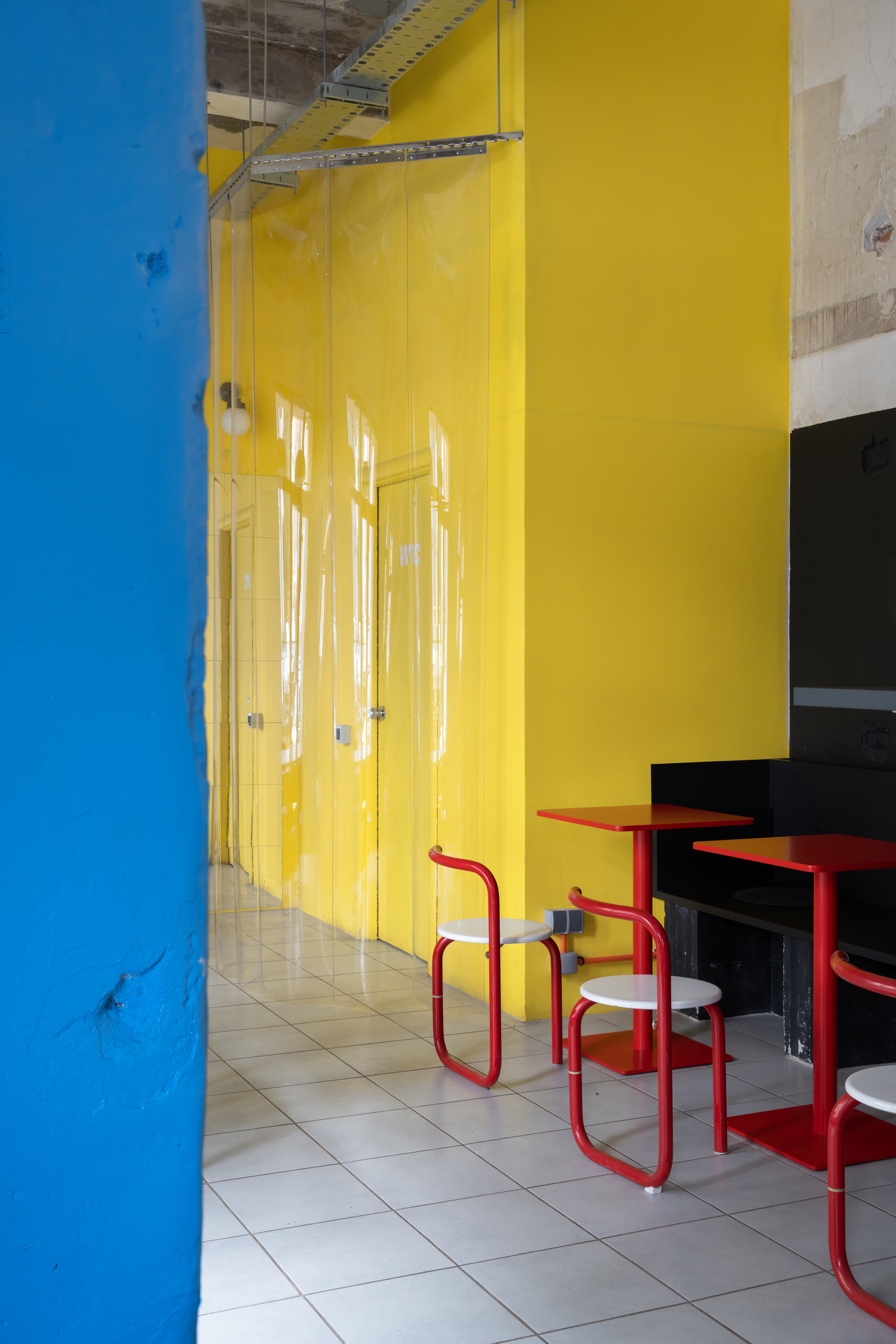Yellow translucent divider wall with exposed ductwork above red metal chairs on cream tile floor