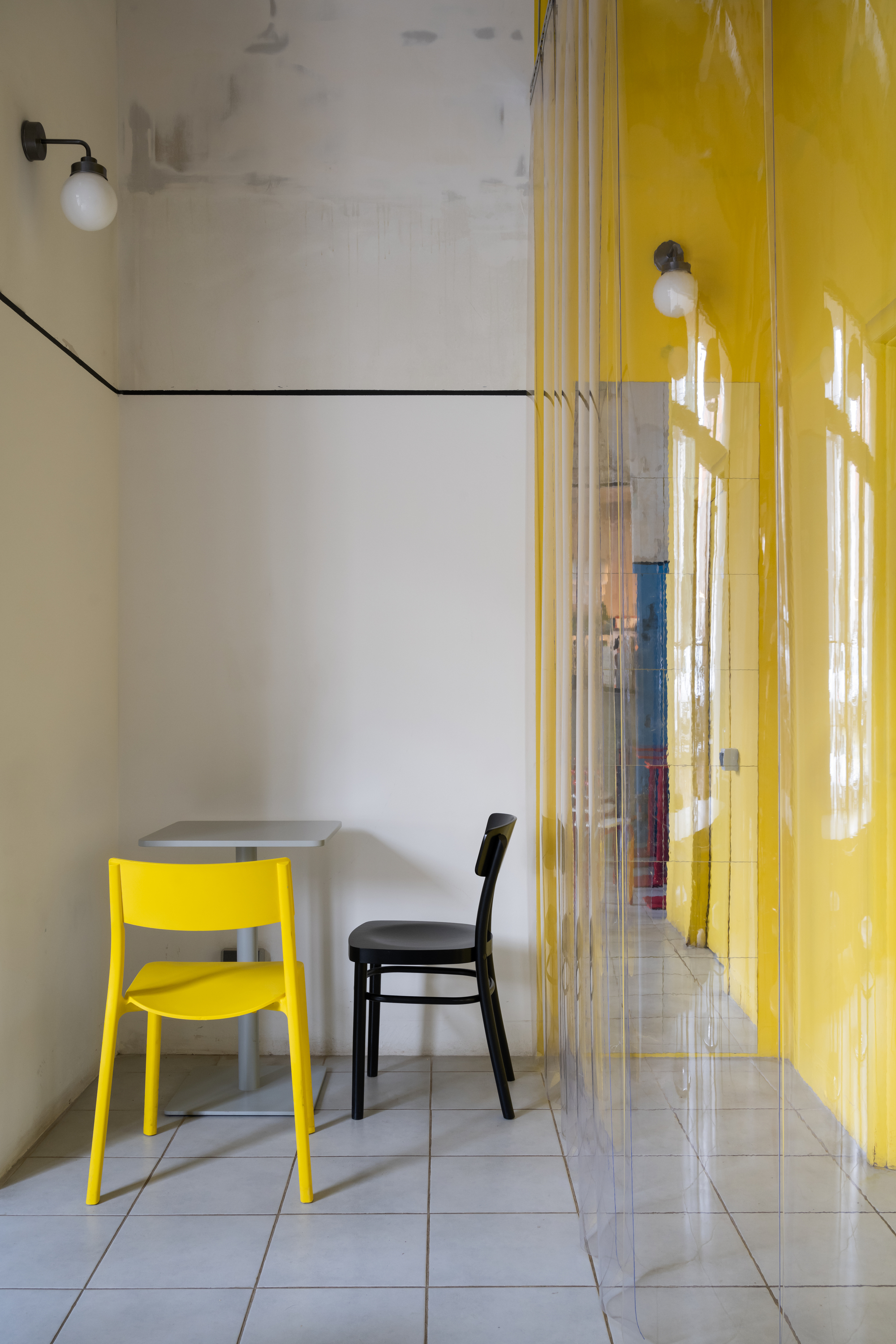 Corner seating nook with yellow and black chairs against white tile wall and translucent yellow curtain
