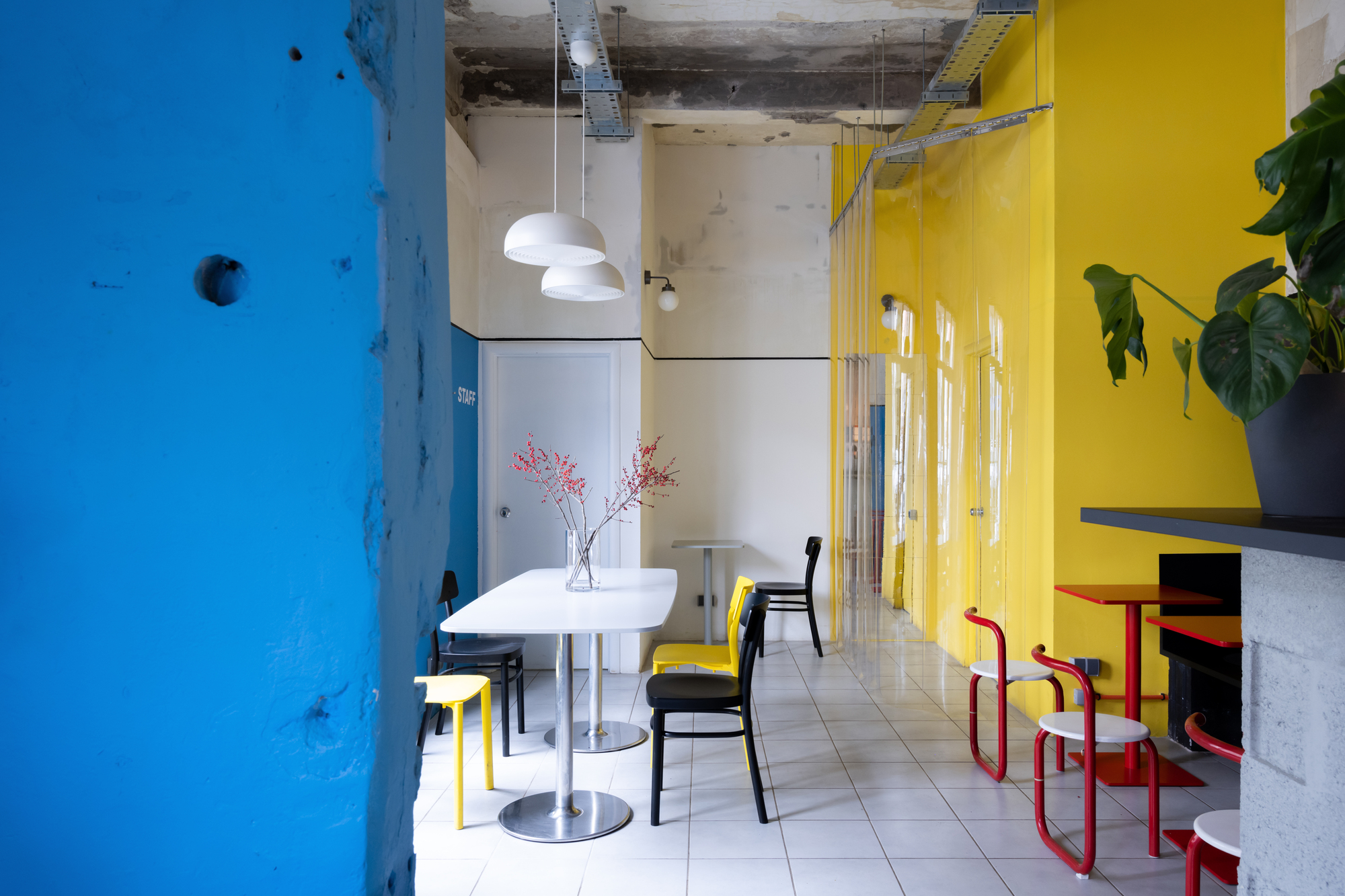 Dining area showing exposed concrete ceiling with ductwork and yellow translucent curtain dividing the space