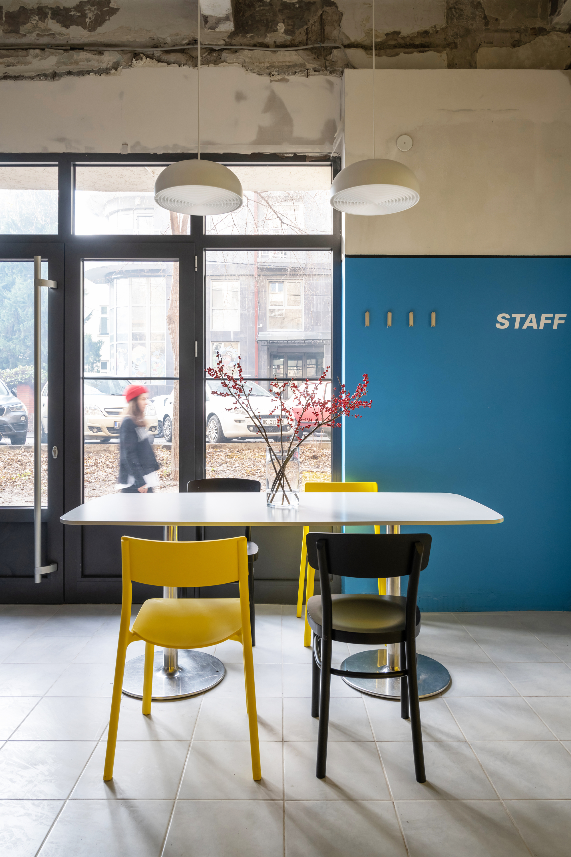 Dining area with white table, yellow and black chairs, and a person walking past the street-facing glazing
