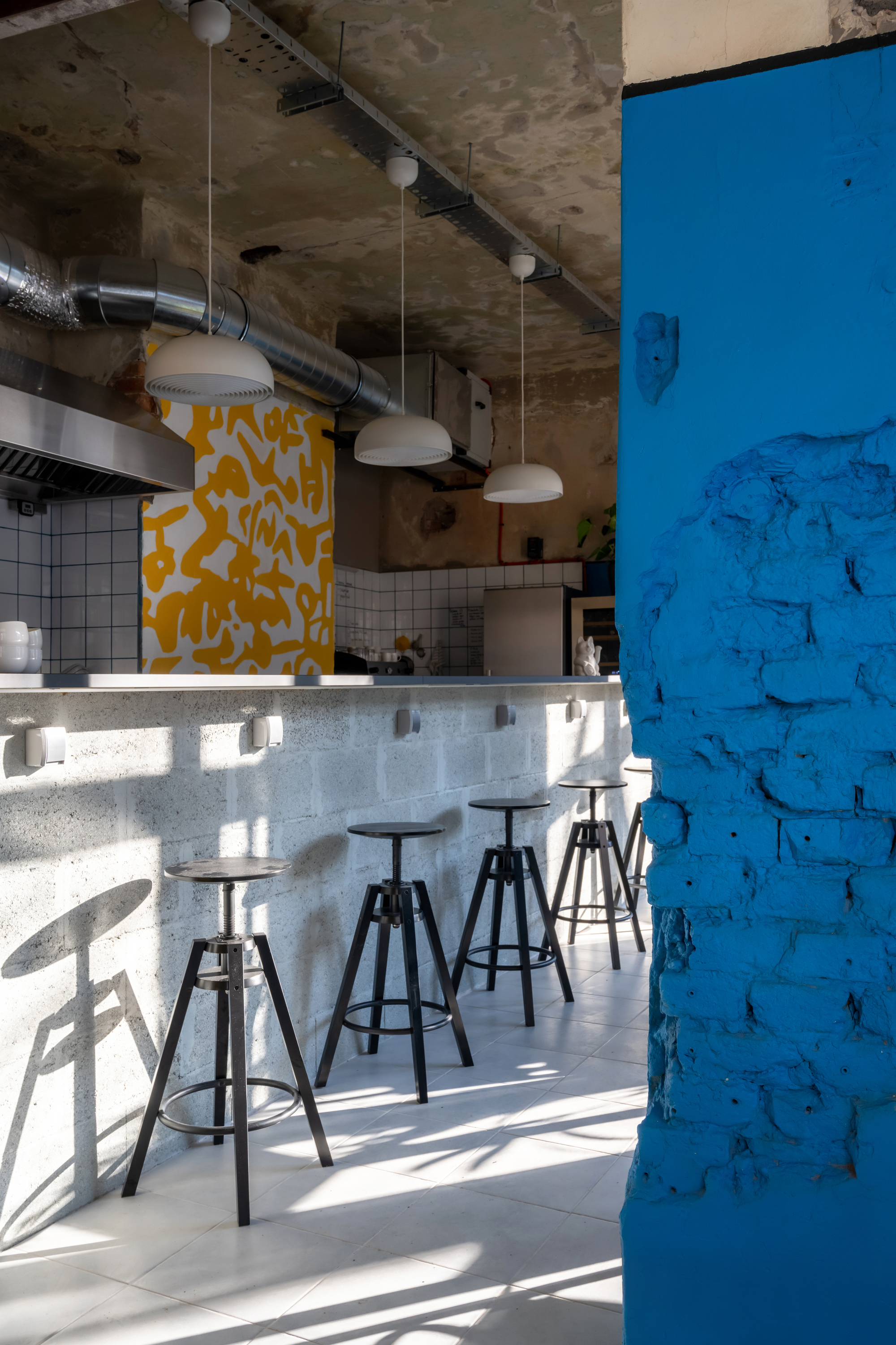 Service counter with adjustable stools beneath exposed concrete ceiling and pendant lights in afternoon sun