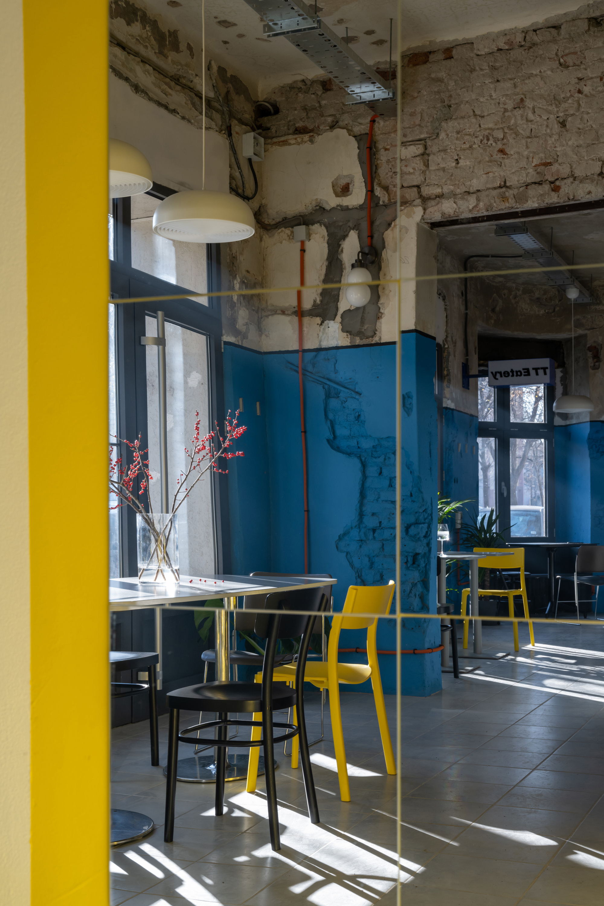 View through yellow-framed glass partition toward dining area with exposed plaster walls and blue wainscoting