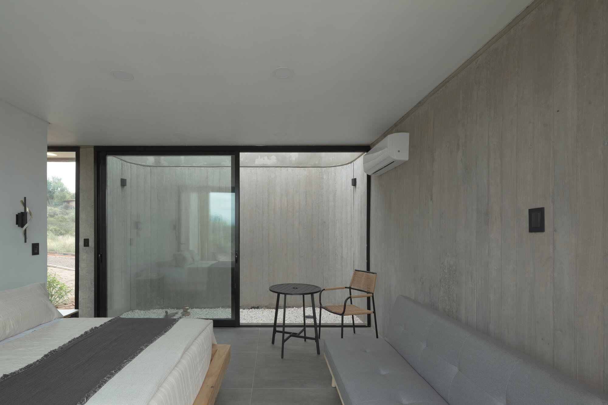 Bedroom with boardformed concrete walls and a glazed corner opening to a private courtyard