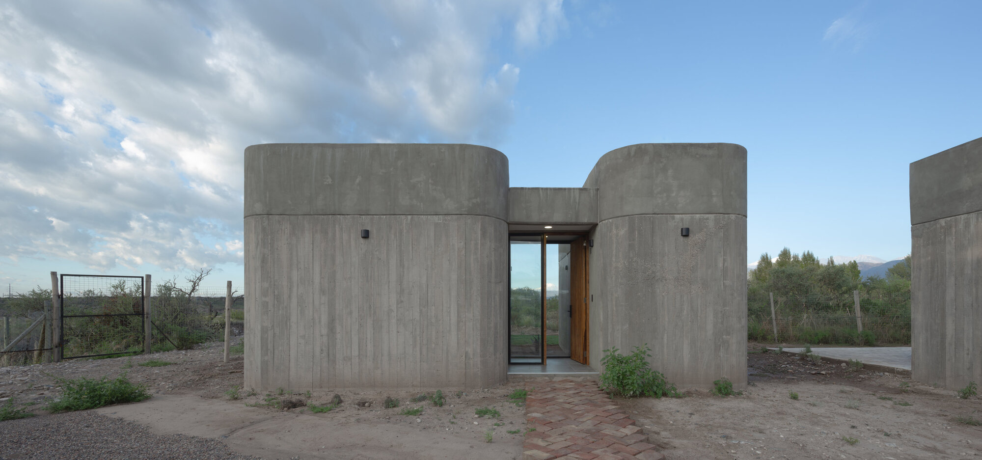 Cylindrical concrete volumes flanking a recessed glass entry in a sparse desert setting
