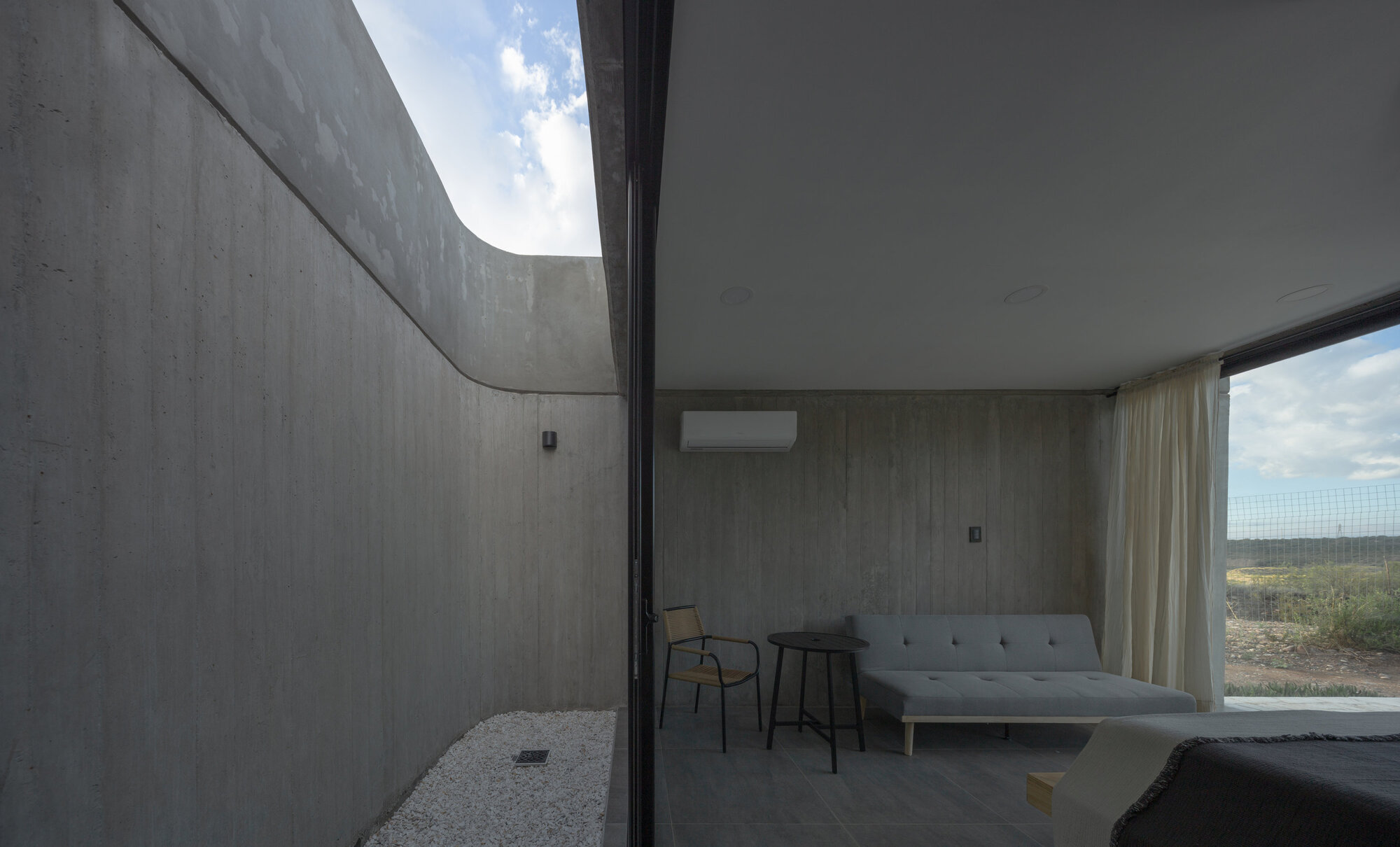 Bedroom interior opening to a private courtyard through floor-to-ceiling glass under an overcast sky