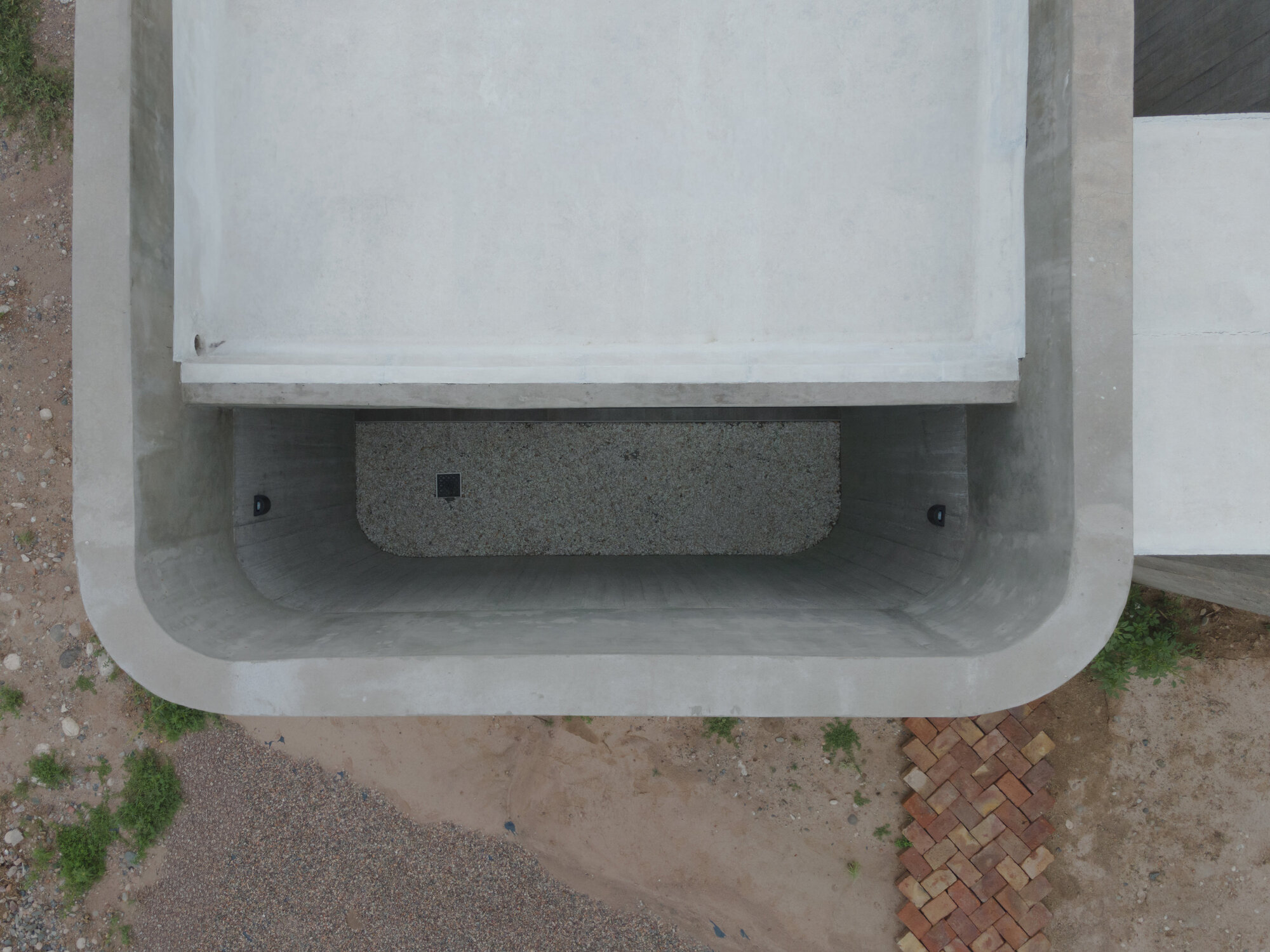 Overhead view of curved concrete canopy sheltering a stone bench and gravel courtyard