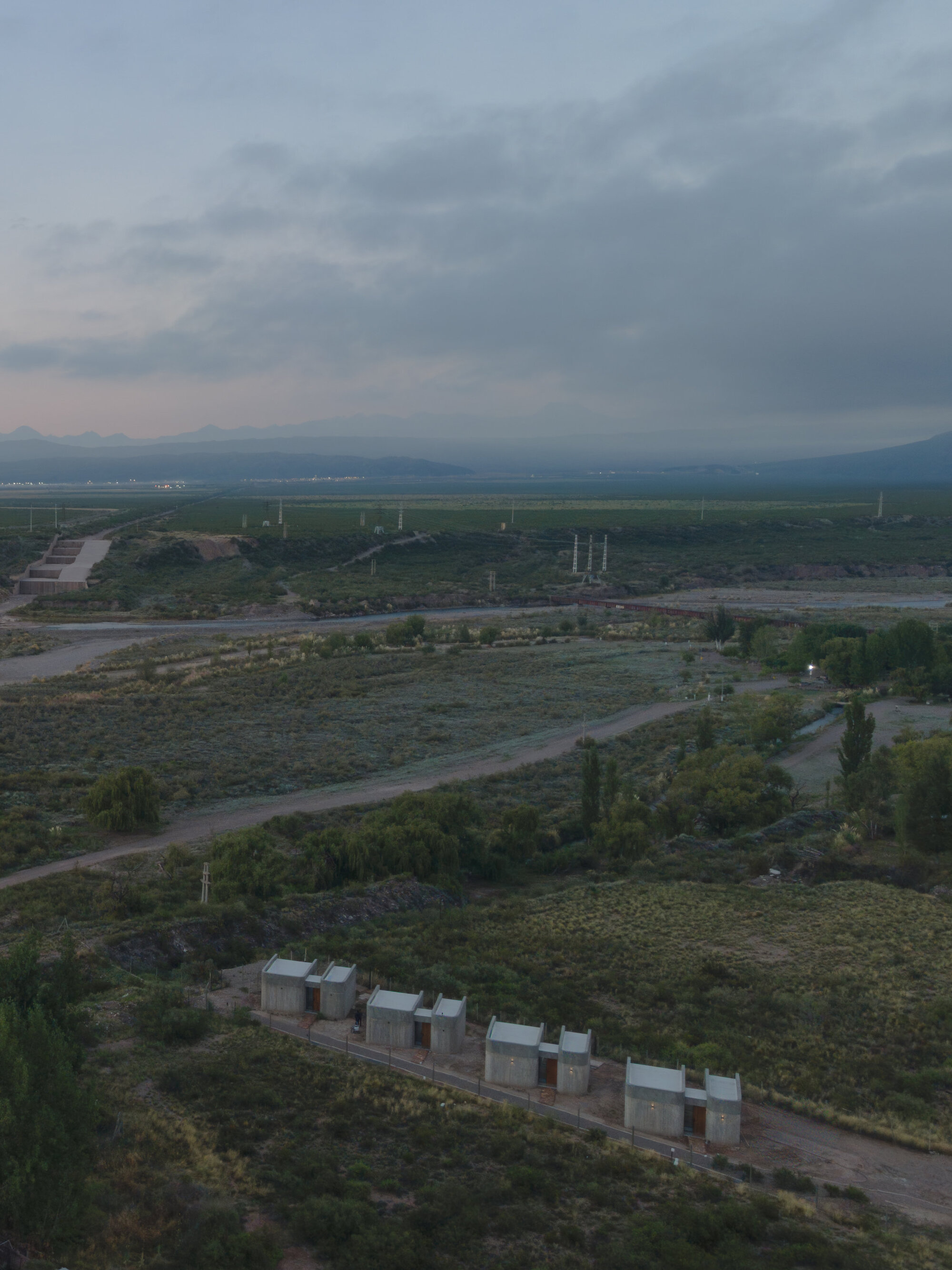 Aerial view of concrete volumes aligned in scrubland at dusk with distant fields and mountains