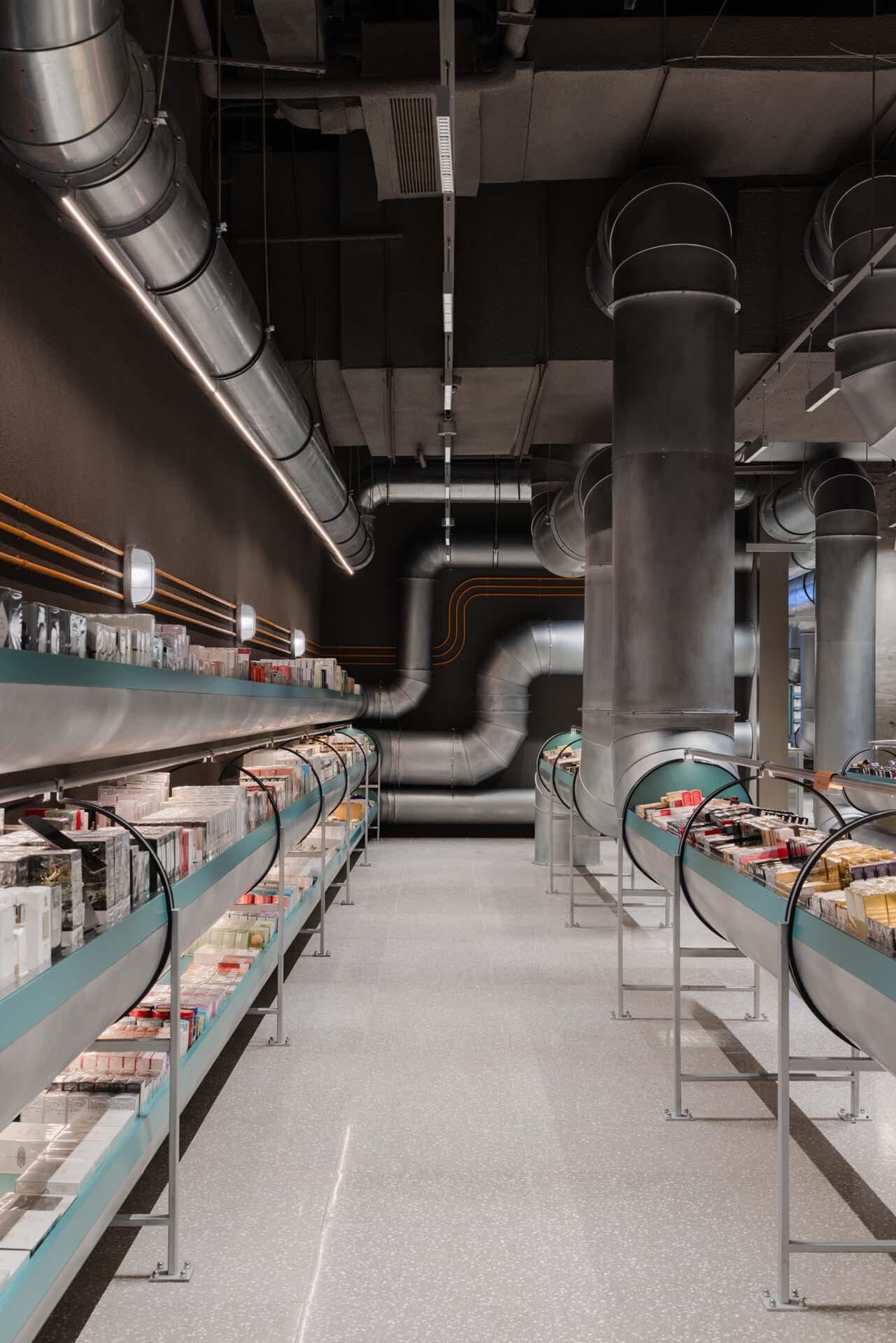 Retail interior with exposed metal ductwork threading between turquoise display shelves and cylindrical columns