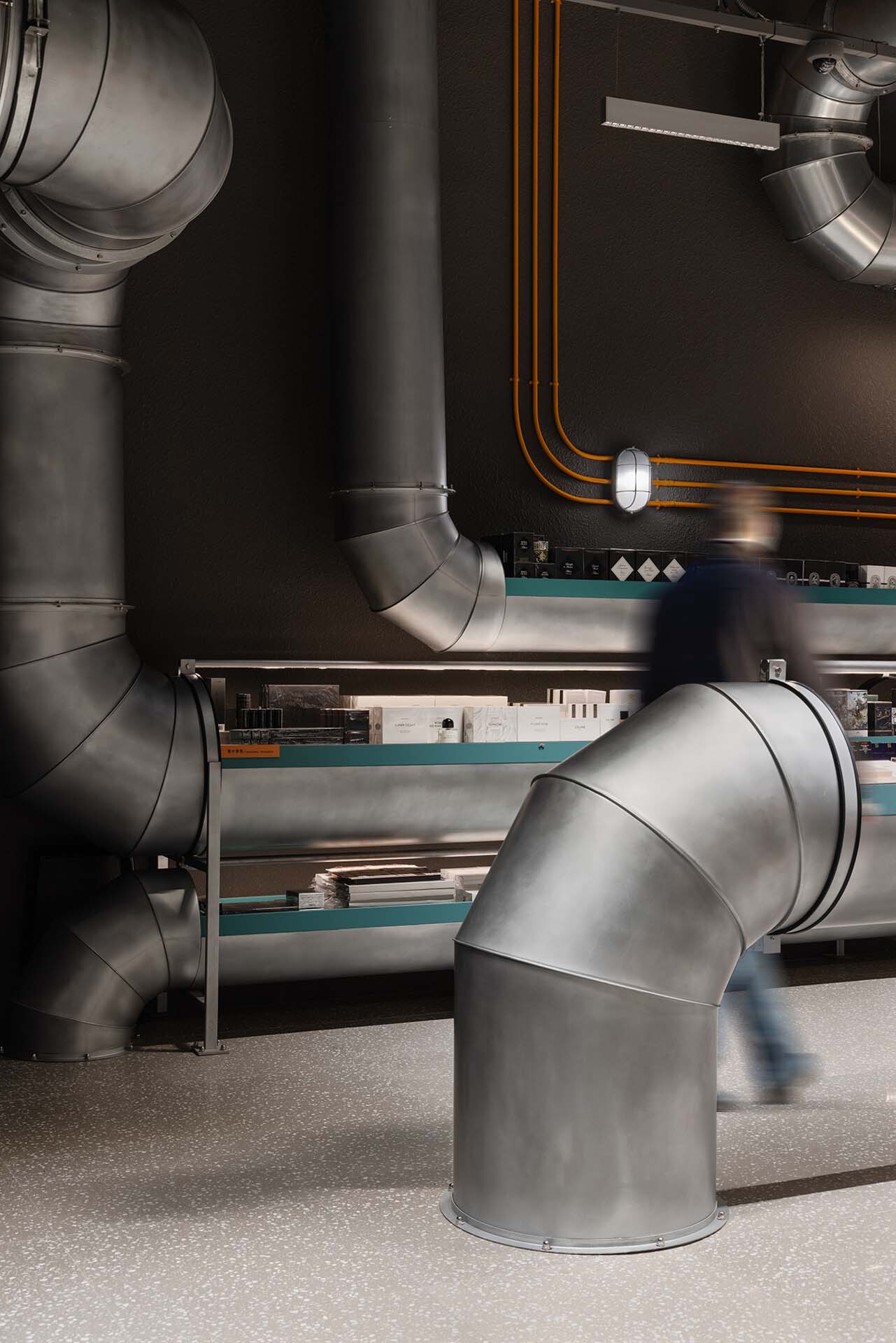 Close-up of sculptural elbow joints in the exposed ductwork above turquoise shelving units