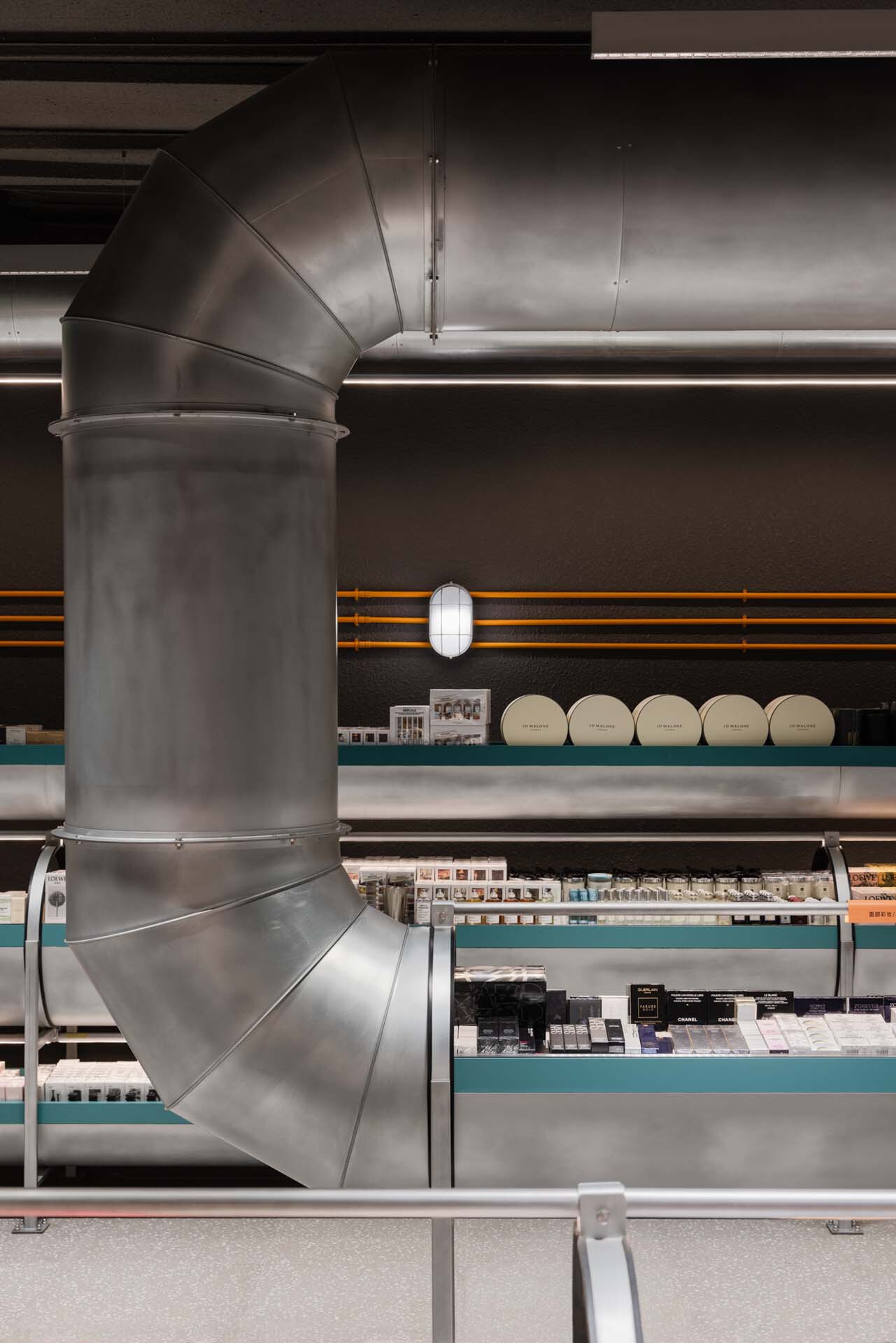 Vertical cylindrical duct rising beside display shelves stocked with packaged goods under artificial lighting