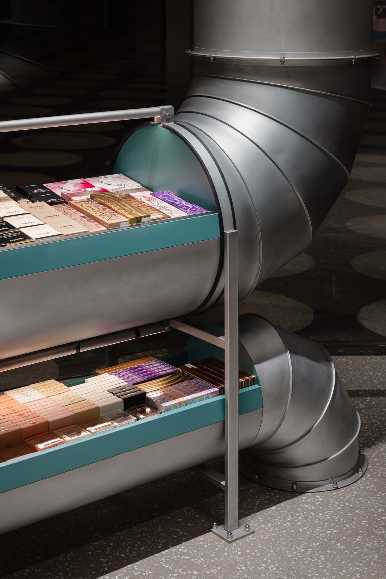 Teal display shelves integrated with round metal ductwork elbows emerging from the floor
