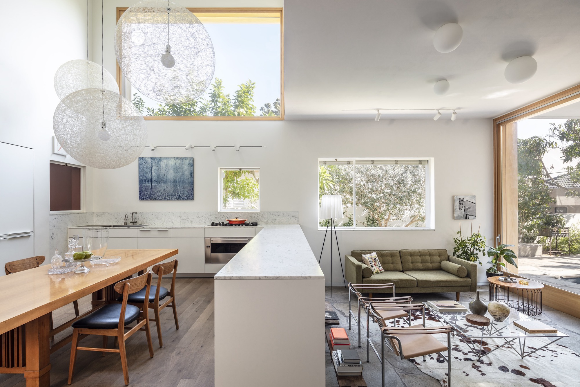Open plan living space with white kitchen island, timber dining table and timber-framed windows overlooking garden