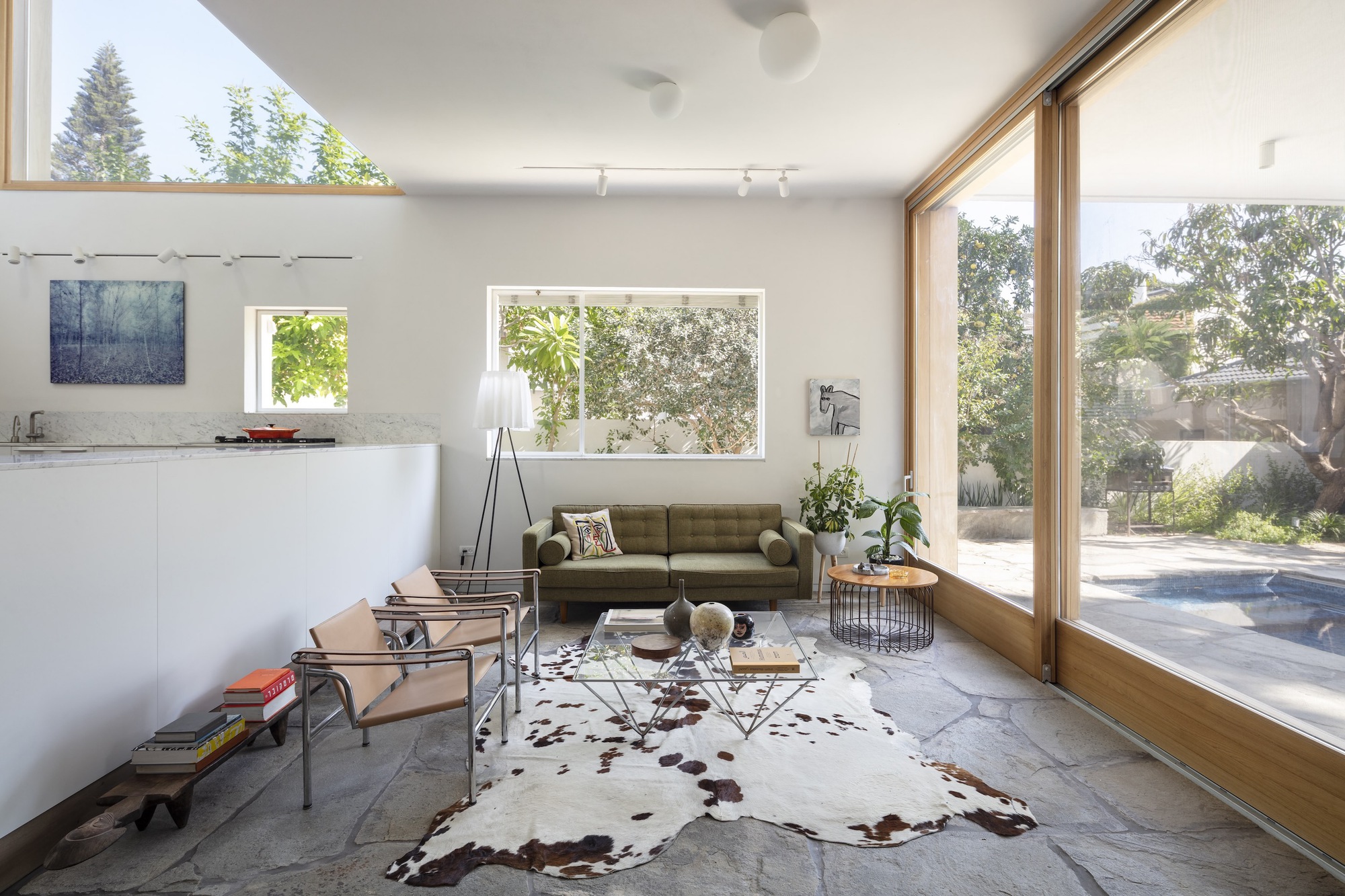 Living room with floor-to-ceiling timber-framed glazing opening to poolside courtyard with established tree