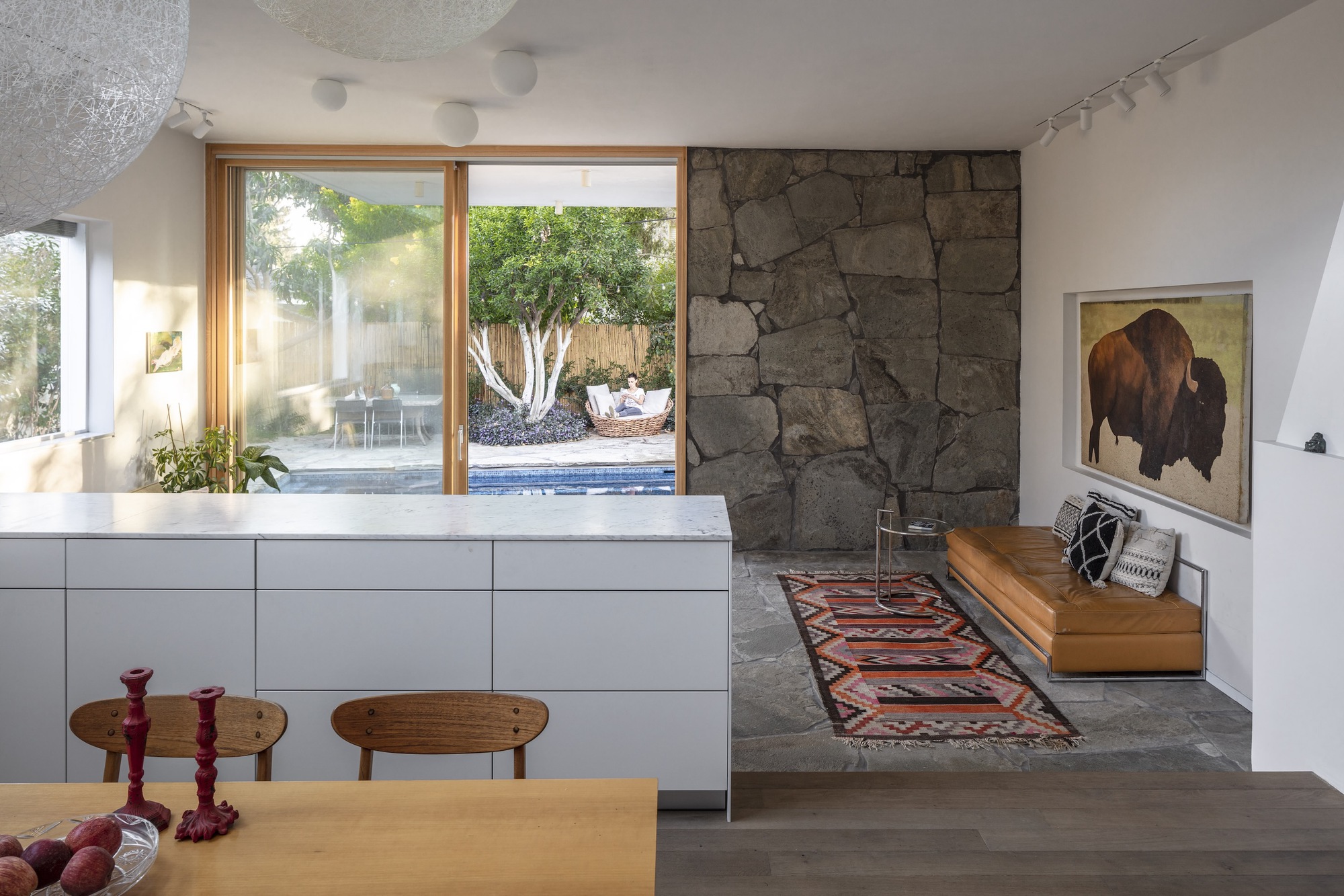 Interior view showing rough stone accent wall beside timber-framed door opening to pool with white-barked tree