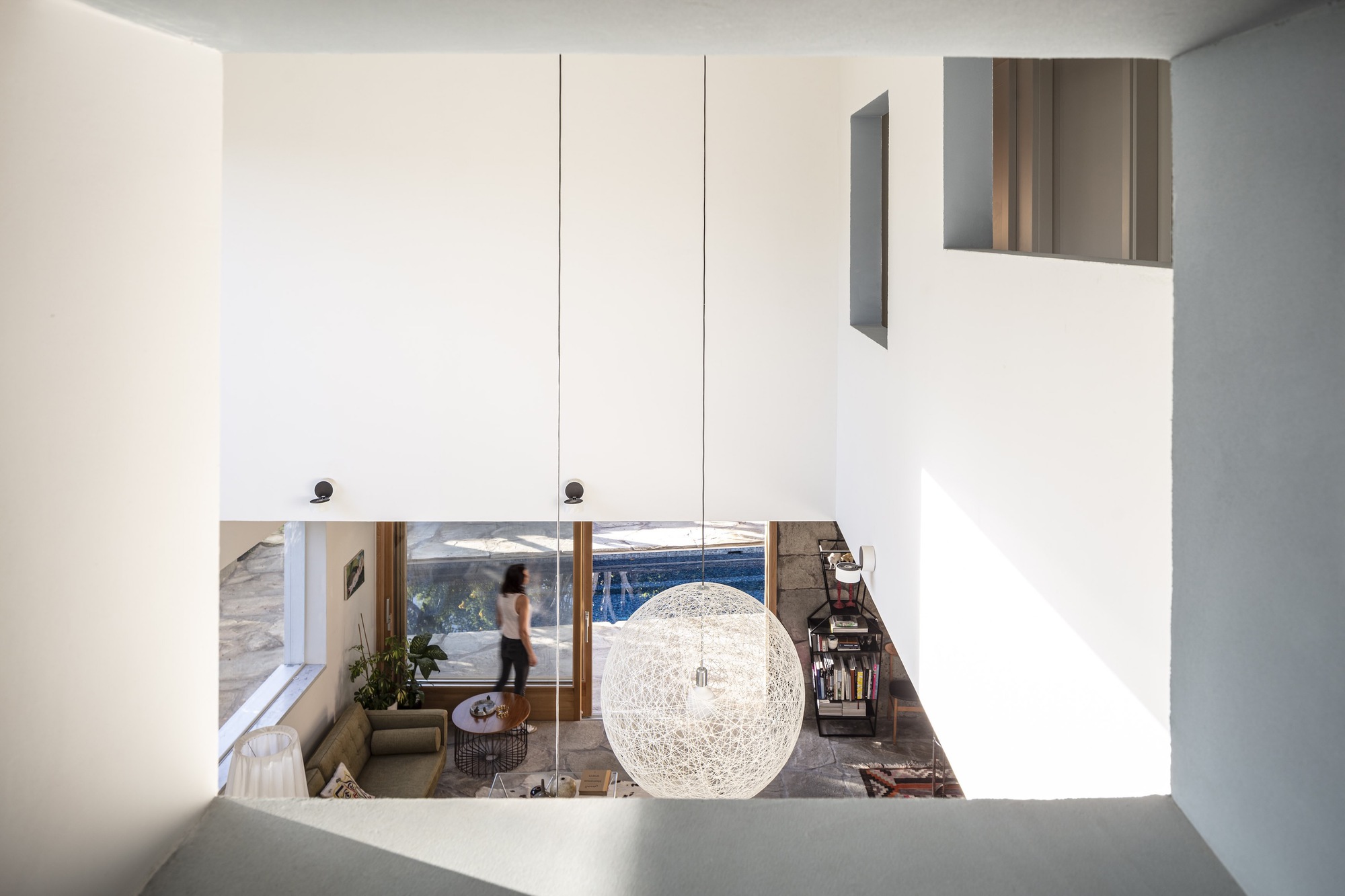 View down from upper level through void showing spherical pendant light and figure in living space below