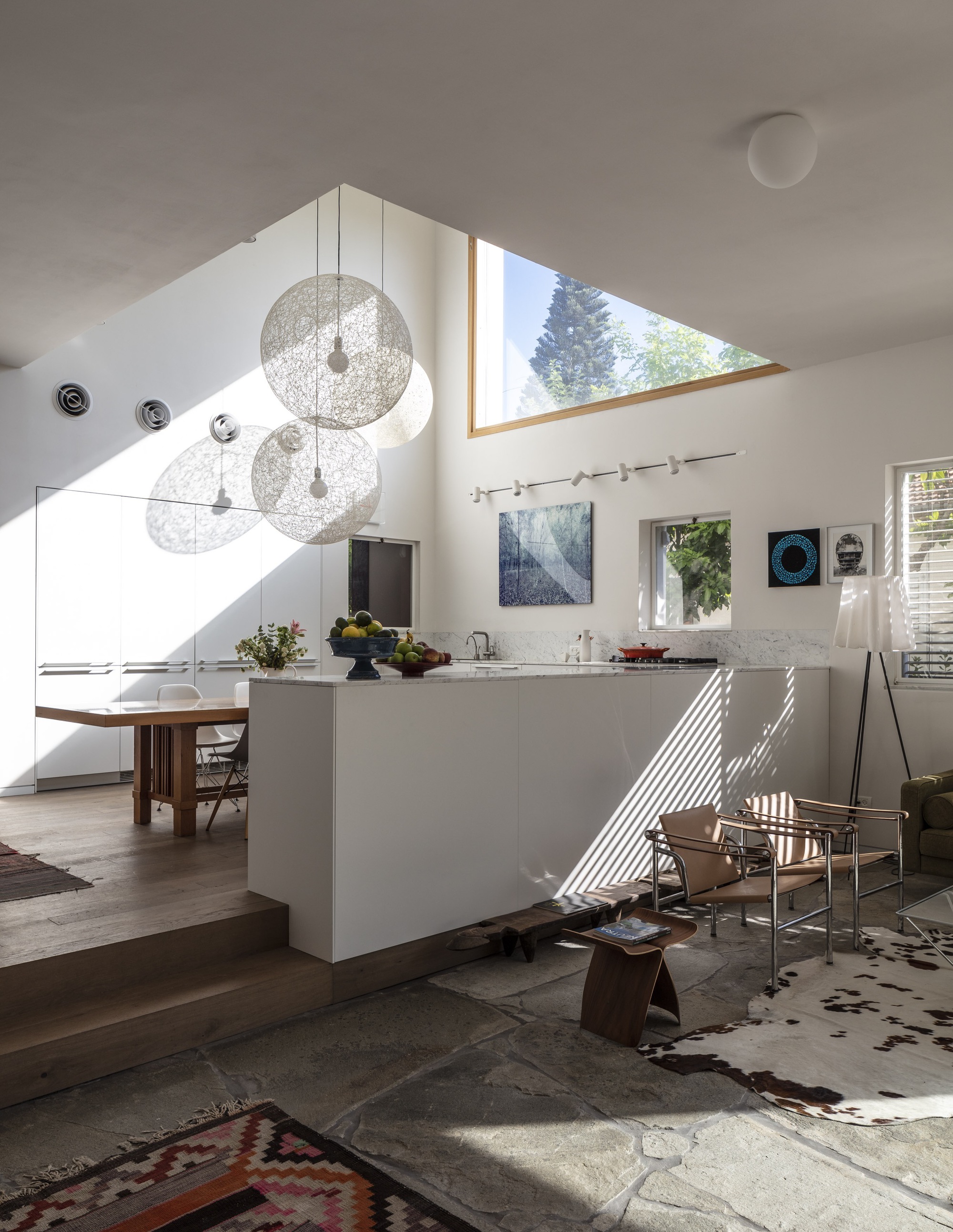 Open kitchen and living area with white island and triangular skylight casting afternoon shadows