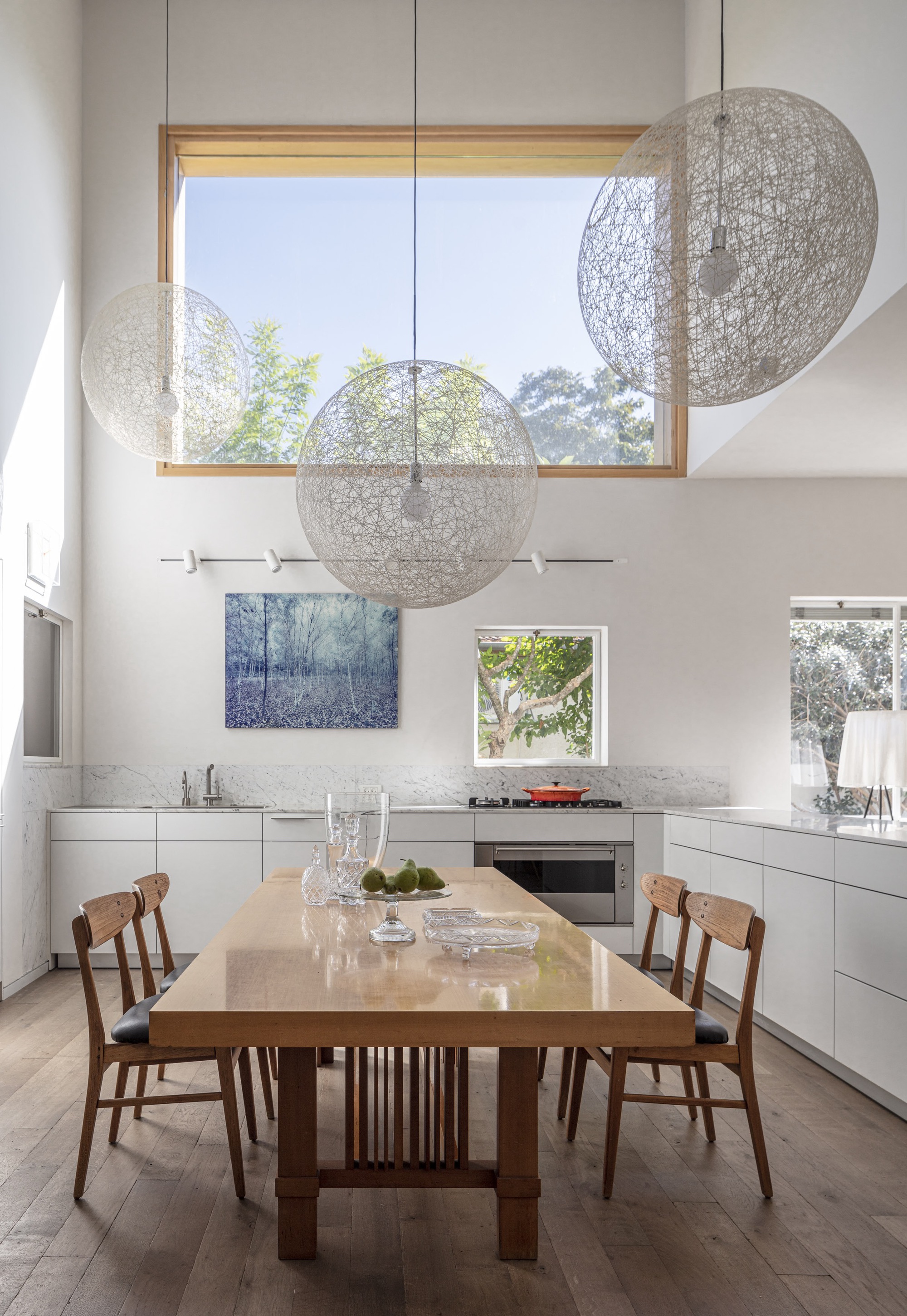 Dining table beneath three spherical pendant lights and timber-framed clerestory window
