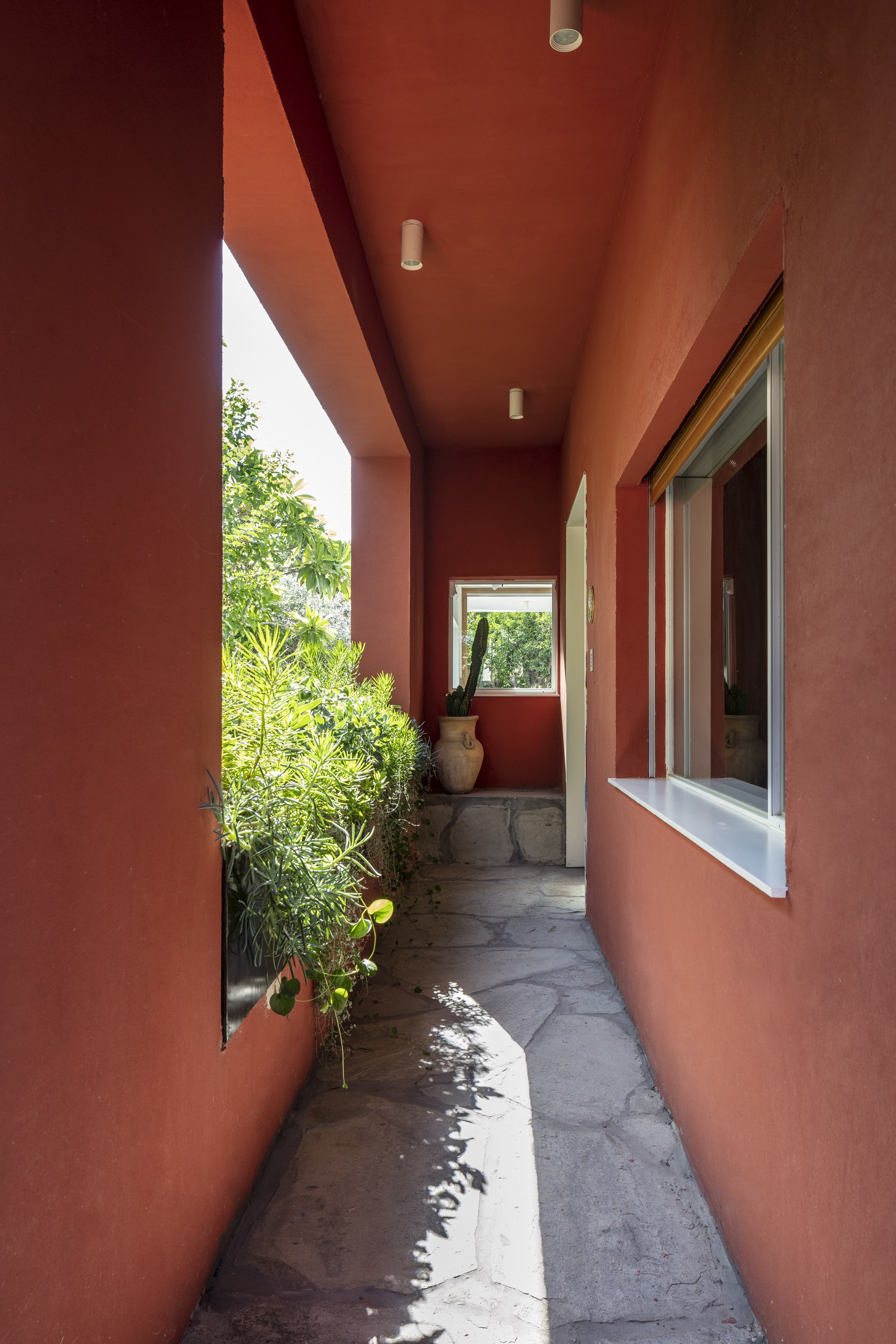 Exterior corridor with terracotta walls and ceiling opening to planted side garden
