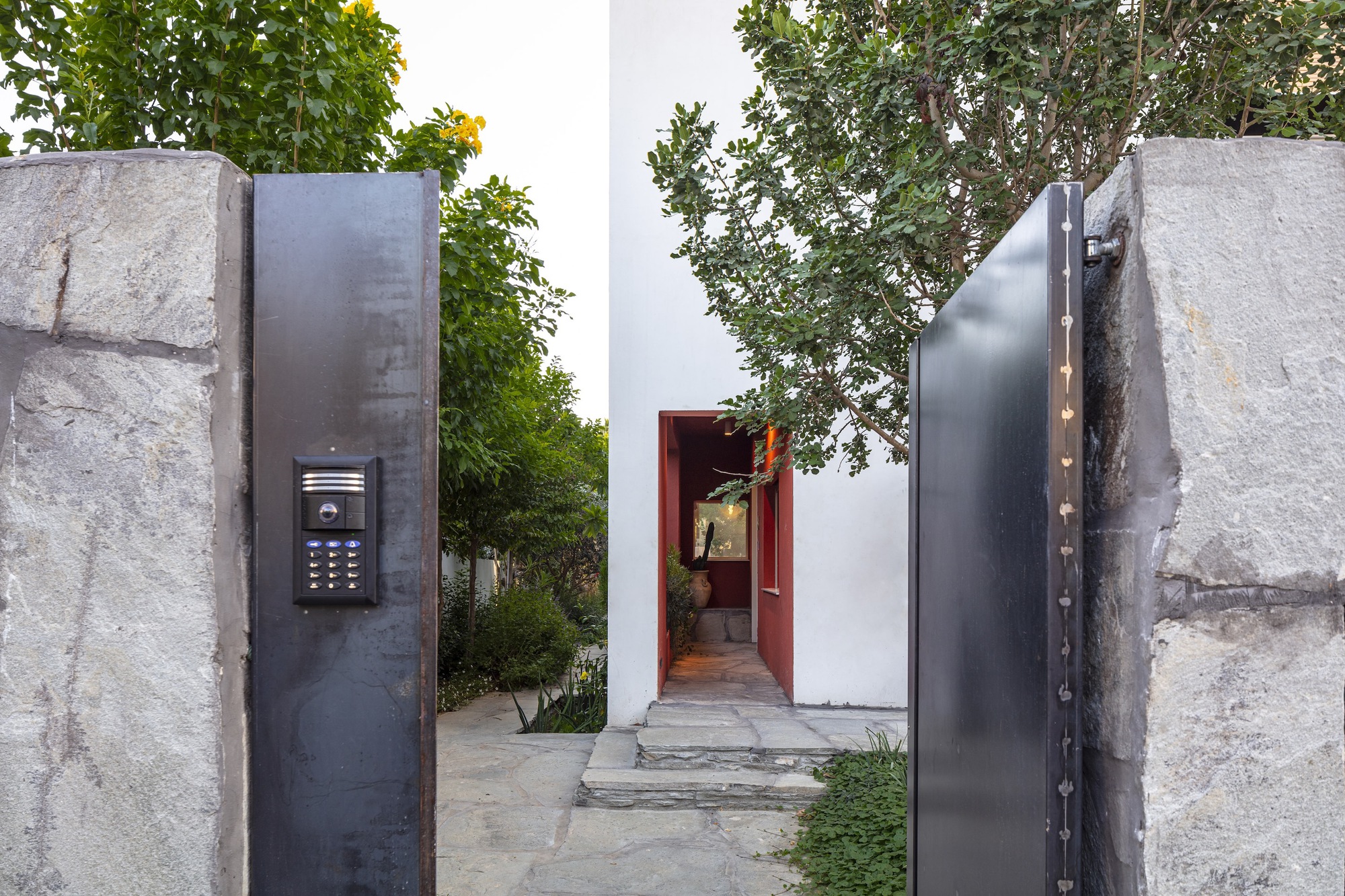 Entry gate with steel panels set between rough stone piers and view to red threshold