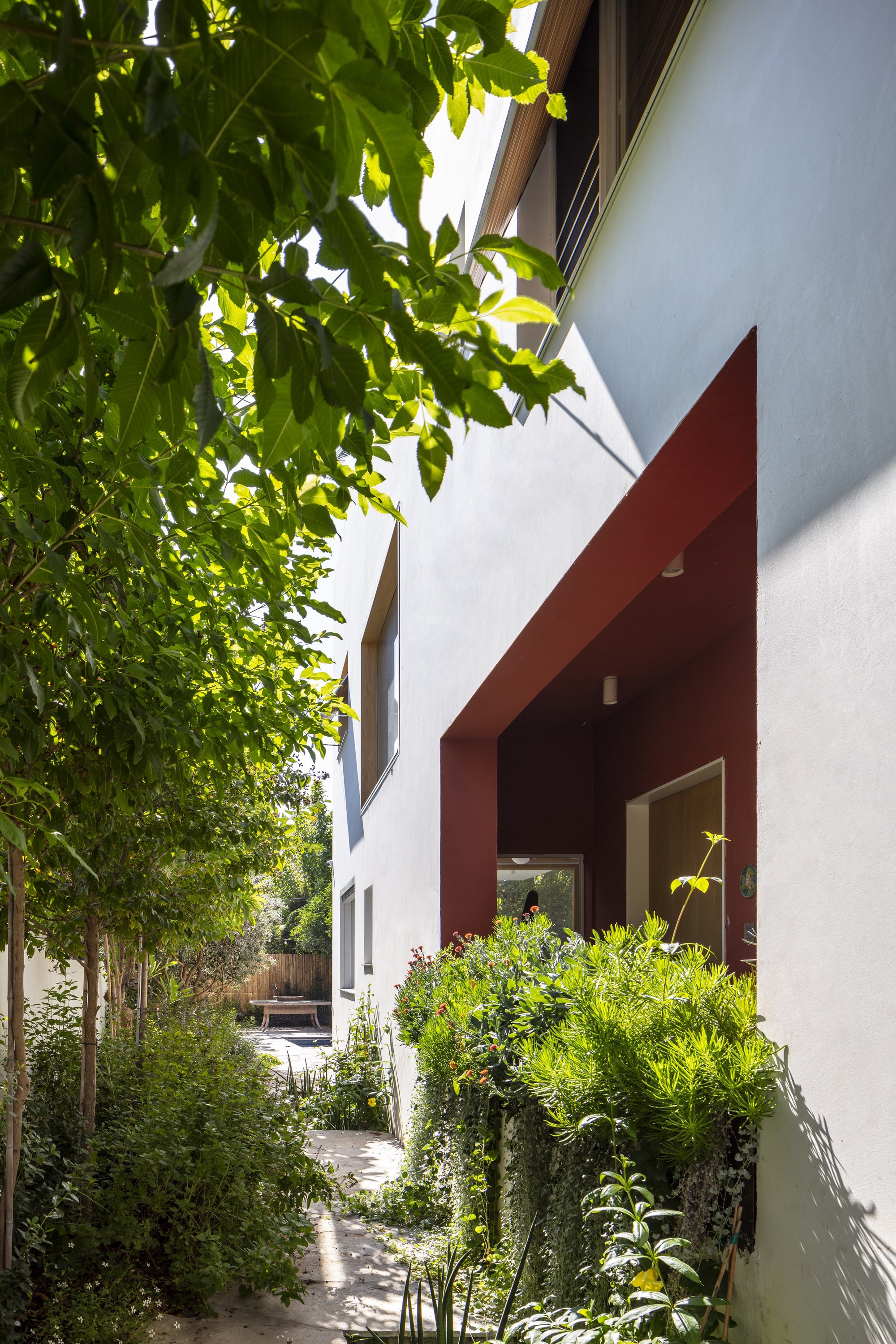 Side passage with red portal frame and white walls beneath overhanging trees in dappled light