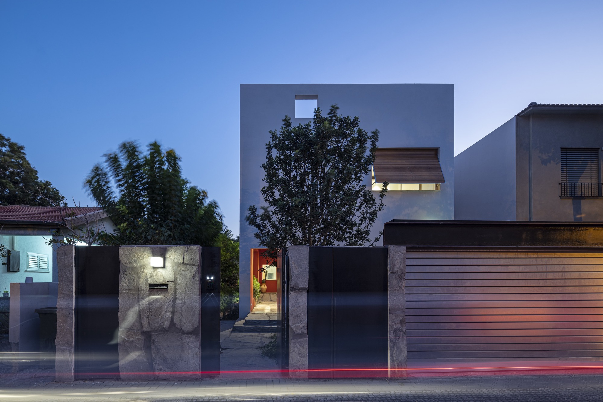 Street facade with black metal gate and gray volumes behind at twilight with light trails