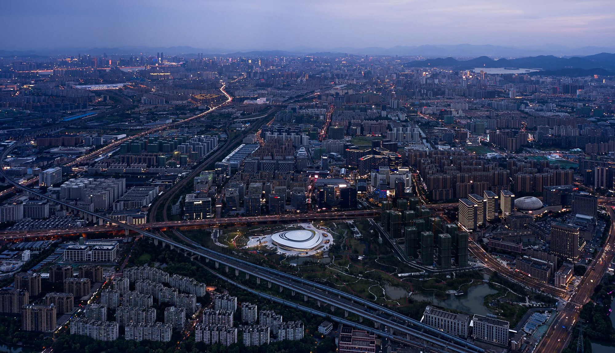 Wide aerial view showing the domed structure within the dense urban grid at blue hour