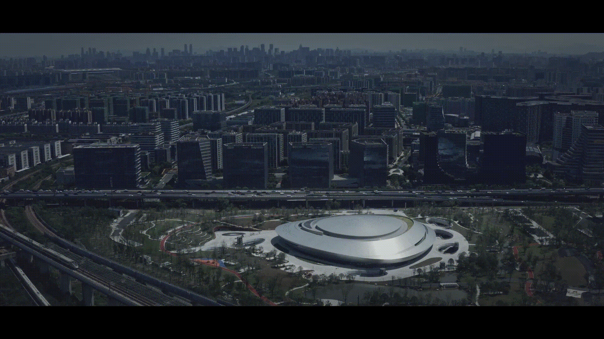 Aerial view of the circular roof amid parkland and urban blocks in afternoon light