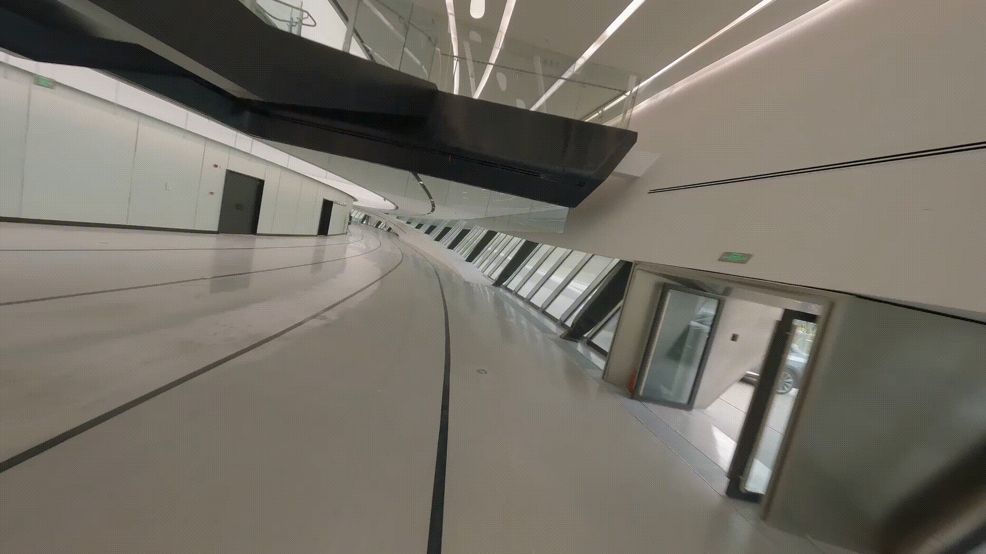 Curving white ramp with escalators and linear ceiling lights in an interior gallery space