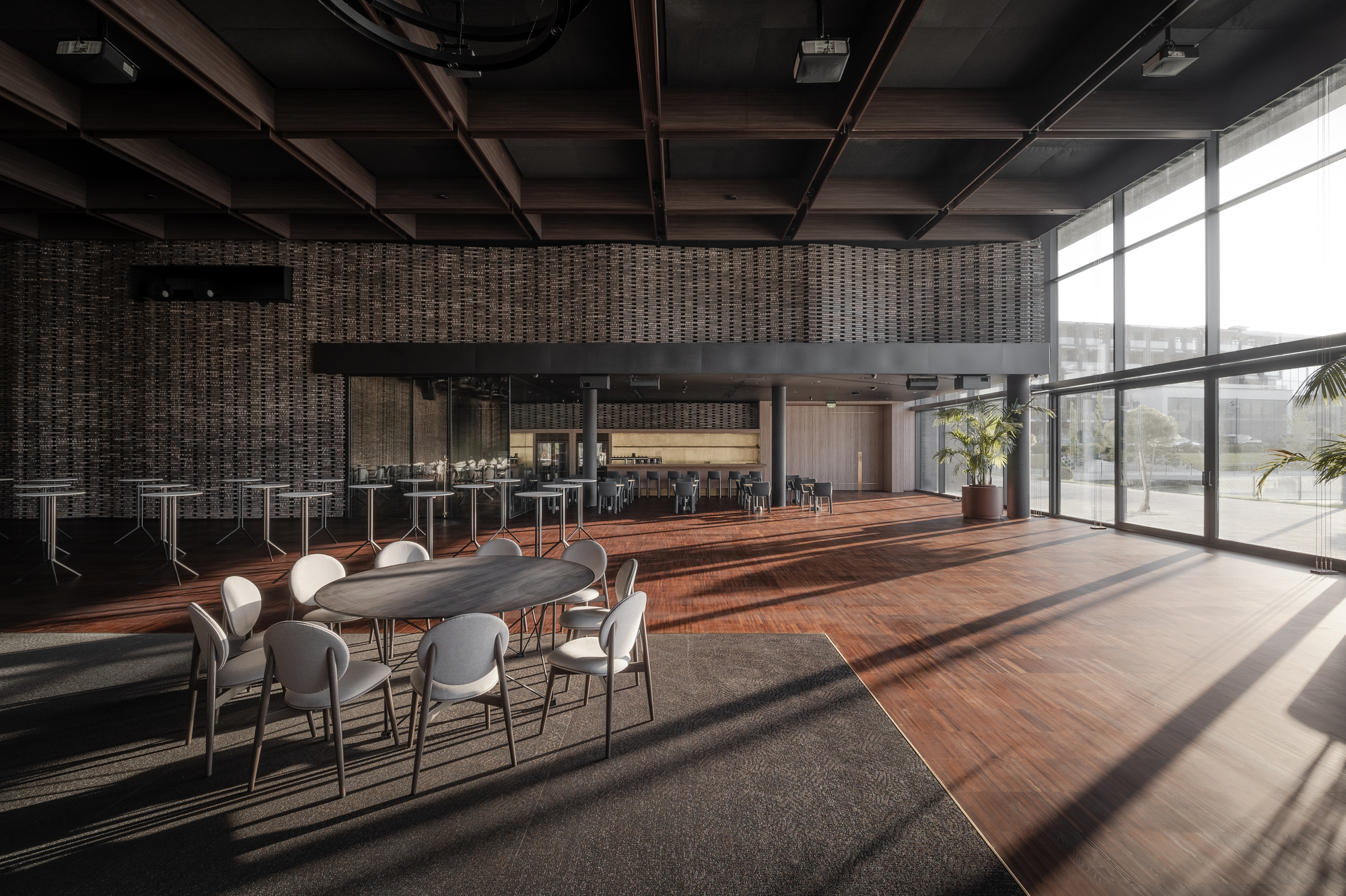 Dining area with exposed timber ceiling beams and floor-to-ceiling windows casting afternoon shadows across hardwood flooring