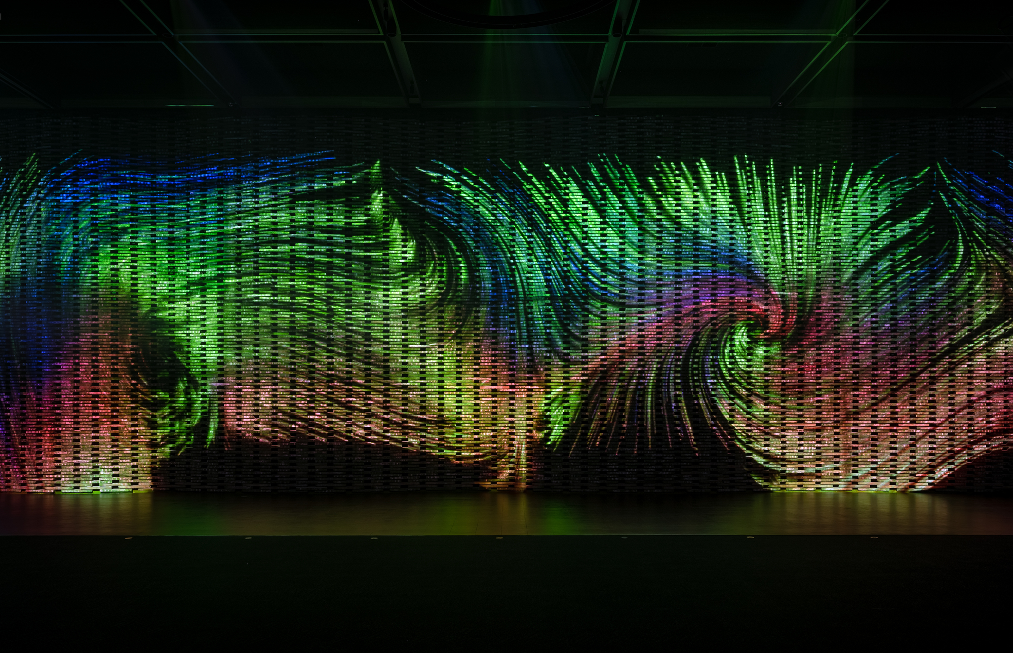 Illuminated undulating screen wall with multicolored LED lighting creating wavelike patterns in darkness