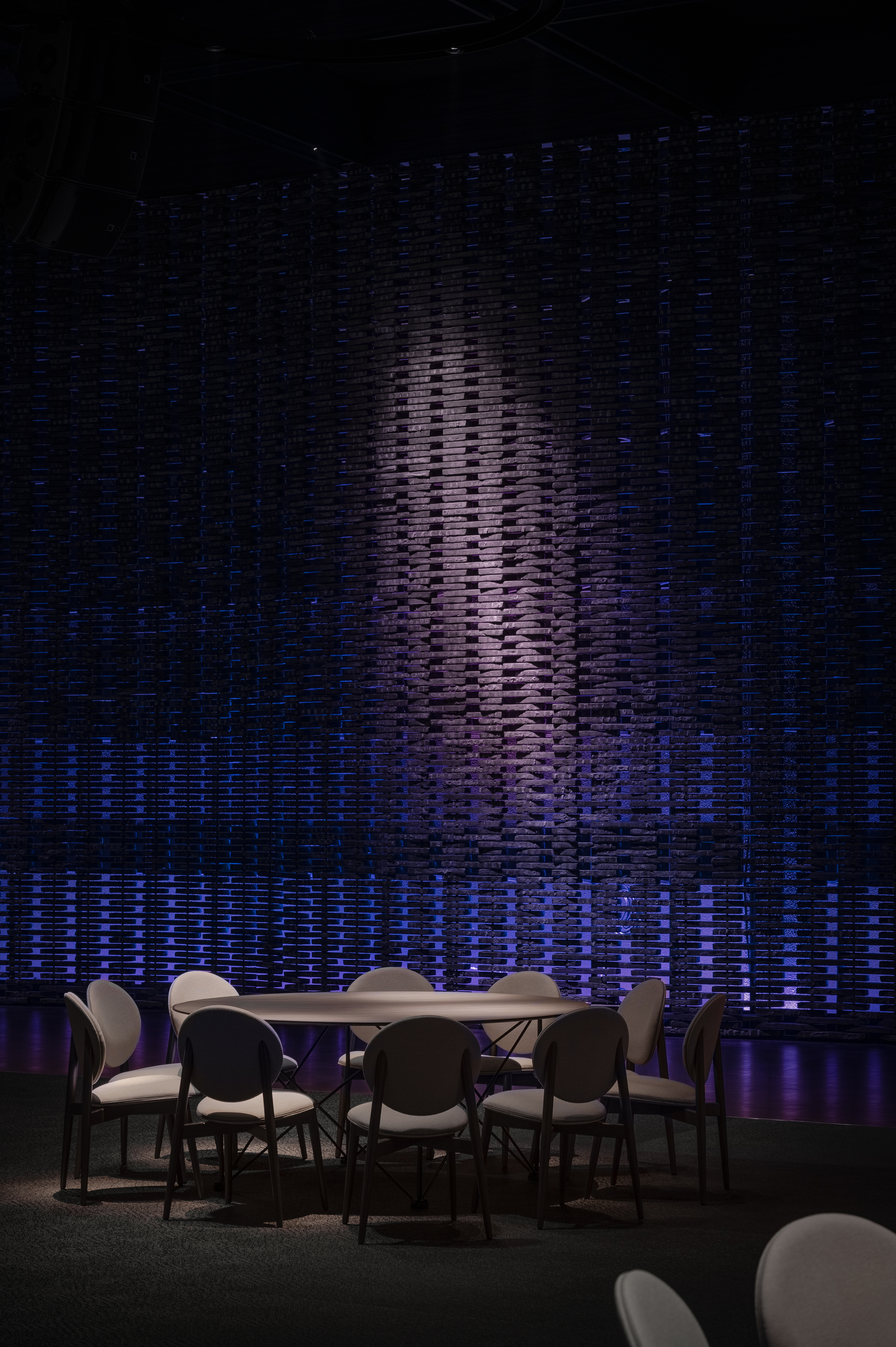 Textured wall installation with vertical relief pattern lit in blue and violet behind a dining table