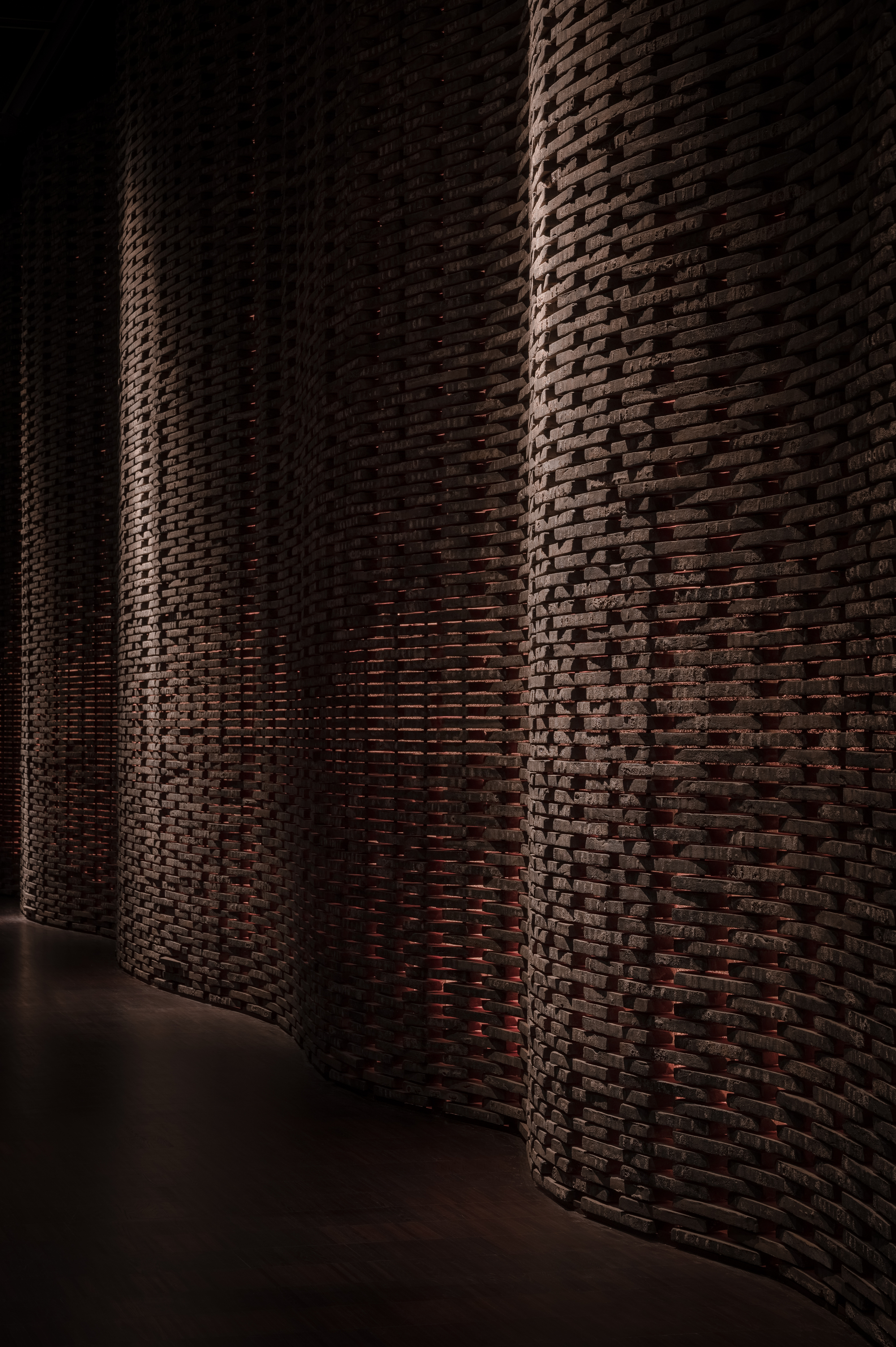 Curving brick wall with basket-weave pattern illuminated by dramatic sidelight in a dark interior corridor