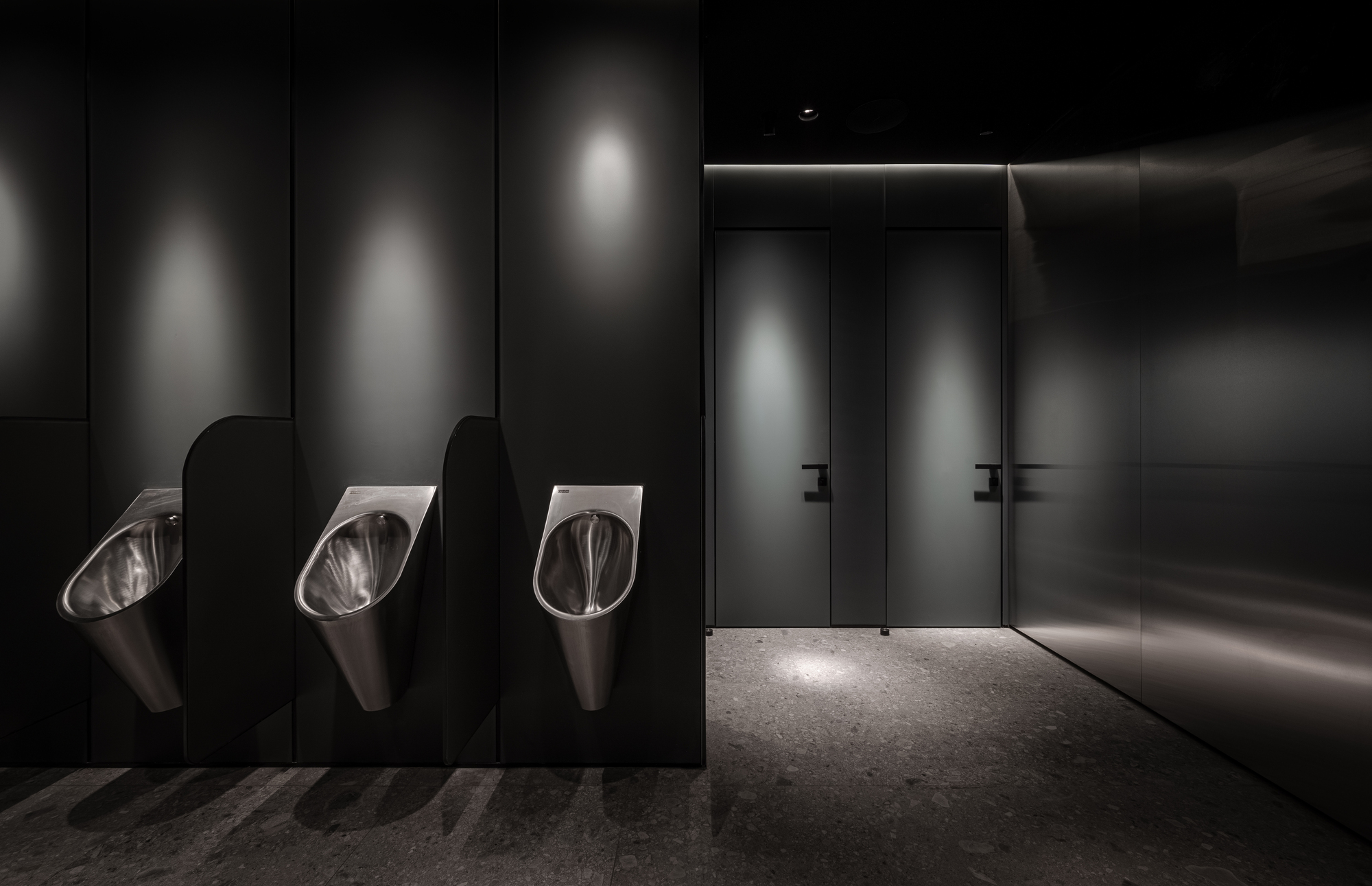 Dark restroom interior with three stainless steel urinals and backlit wall panels