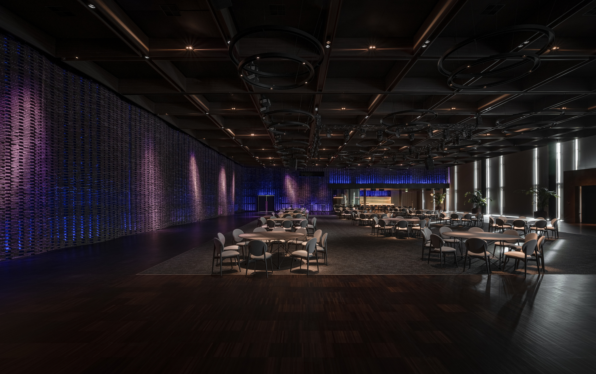 Event hall with woven wall panels illuminated in purple and blue and scattered dining tables