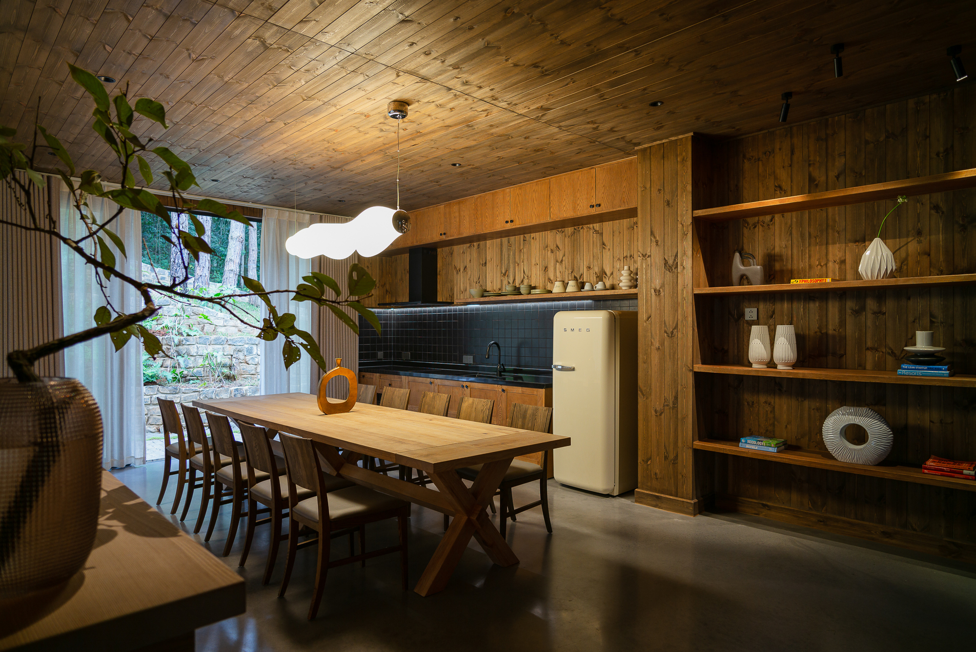 Dining room with vaulted timber ceiling and open shelving beside a glazed courtyard with greenery