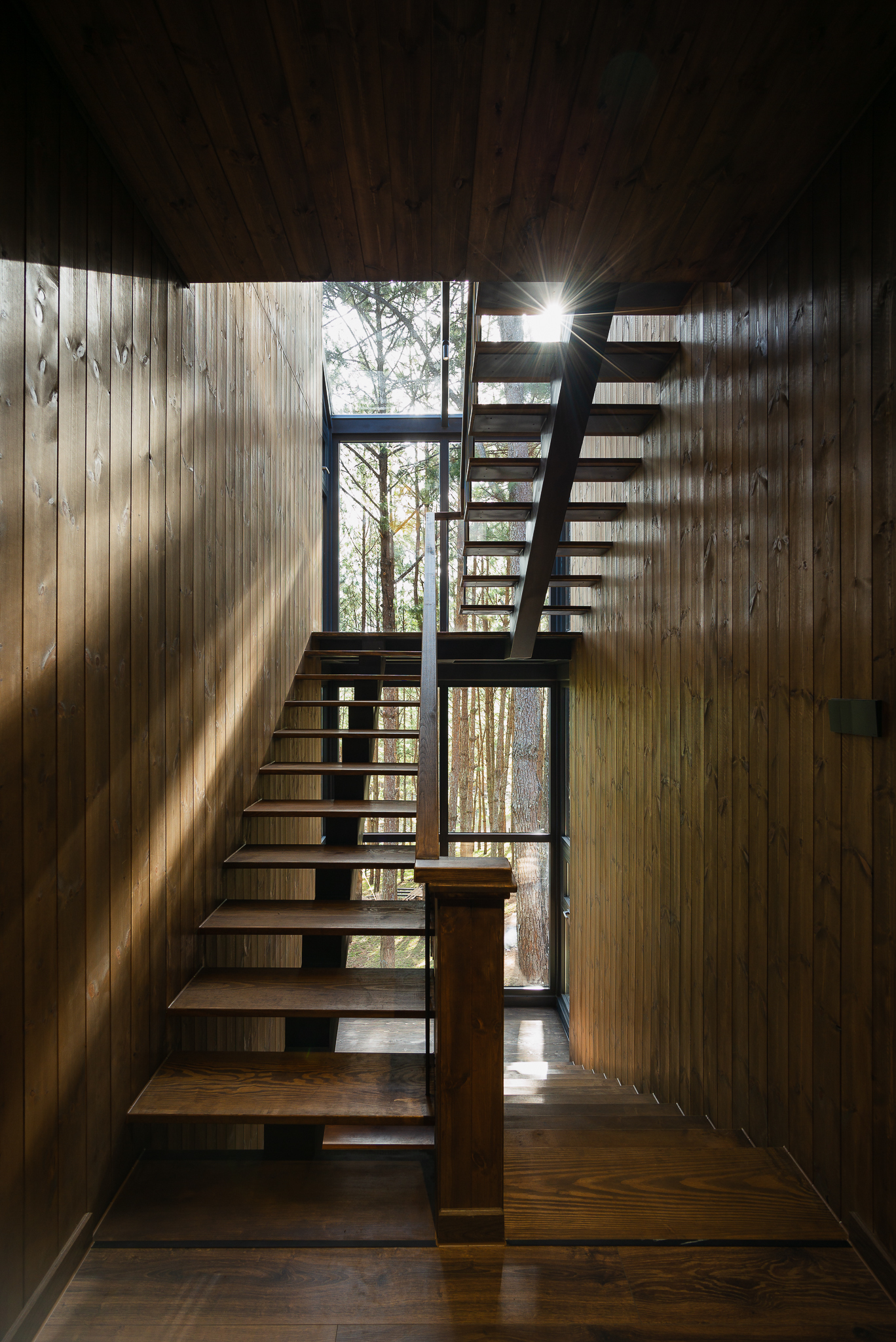 Open timber staircase with slats of sunlight filtering through the vertical wood wall cladding