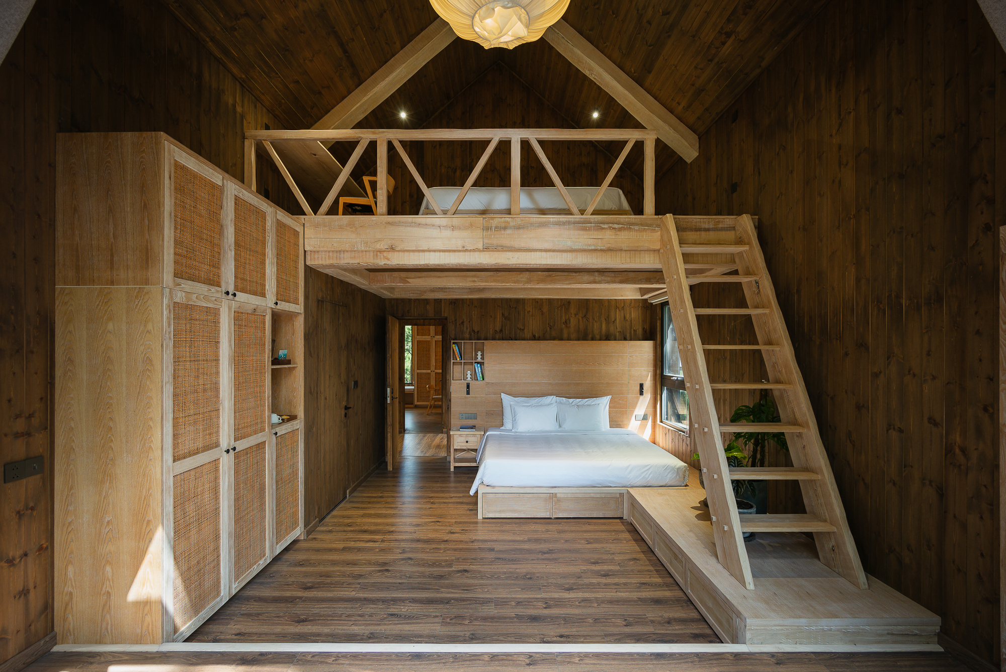 Bedroom with timber loft platform accessed by a ladder beneath an exposed wood rafter ceiling