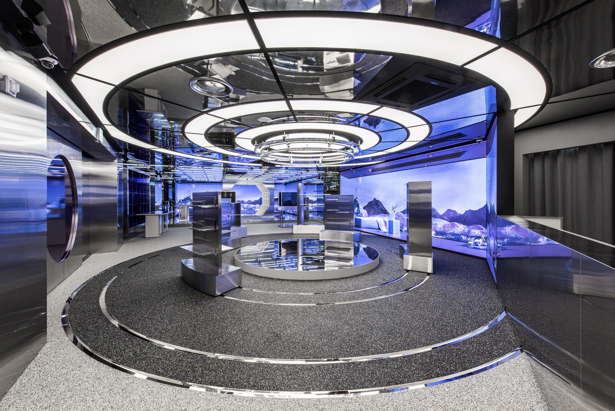 Circular stepped floor under concentric ring light fixtures with blue projected landscape imagery on surrounding walls
