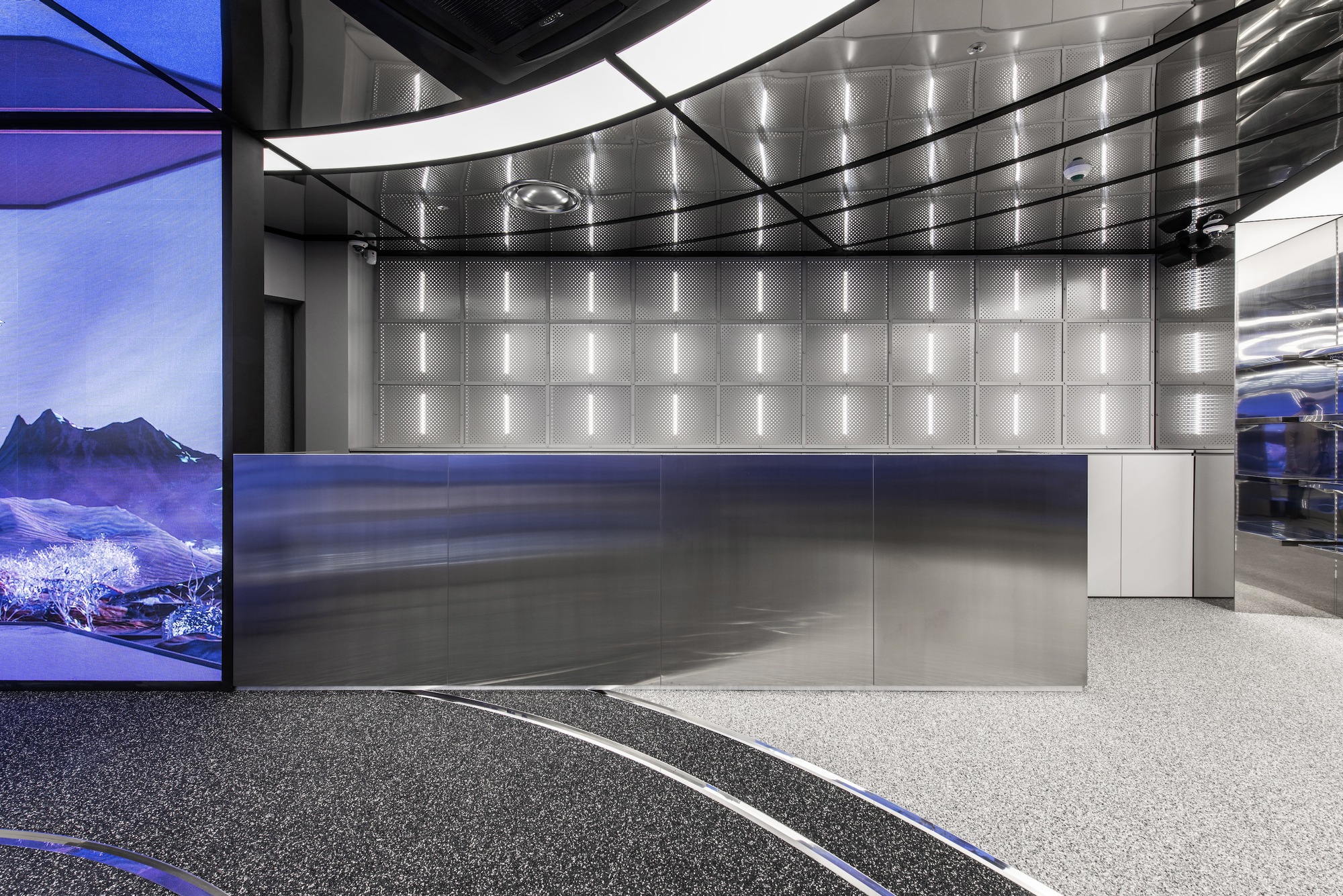 Brushed steel reception desk beneath a quilted metal panel ceiling with recessed linear lighting