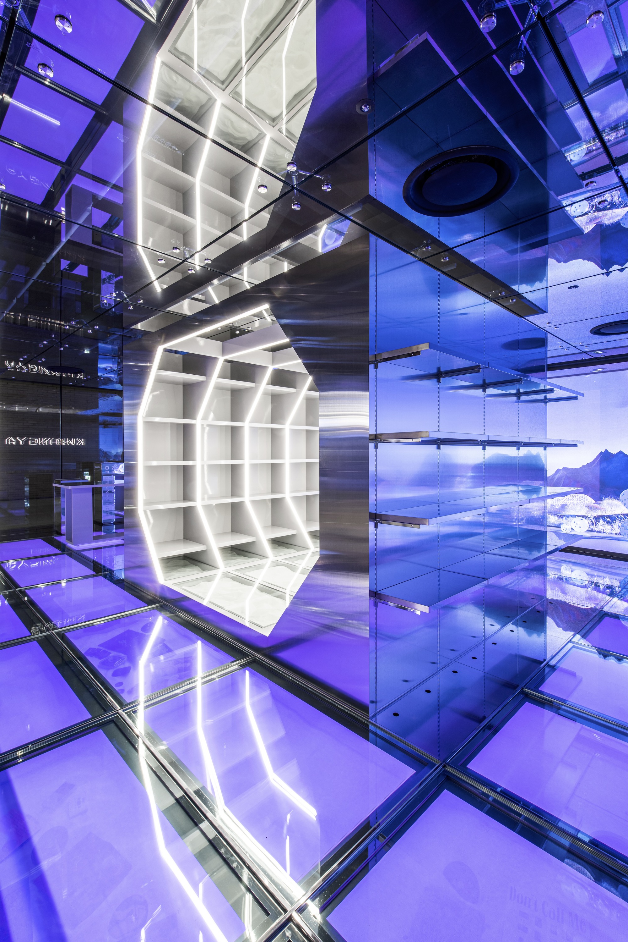 White shelving cube suspended in atrium space with transparent glass floor and blue lit walls
