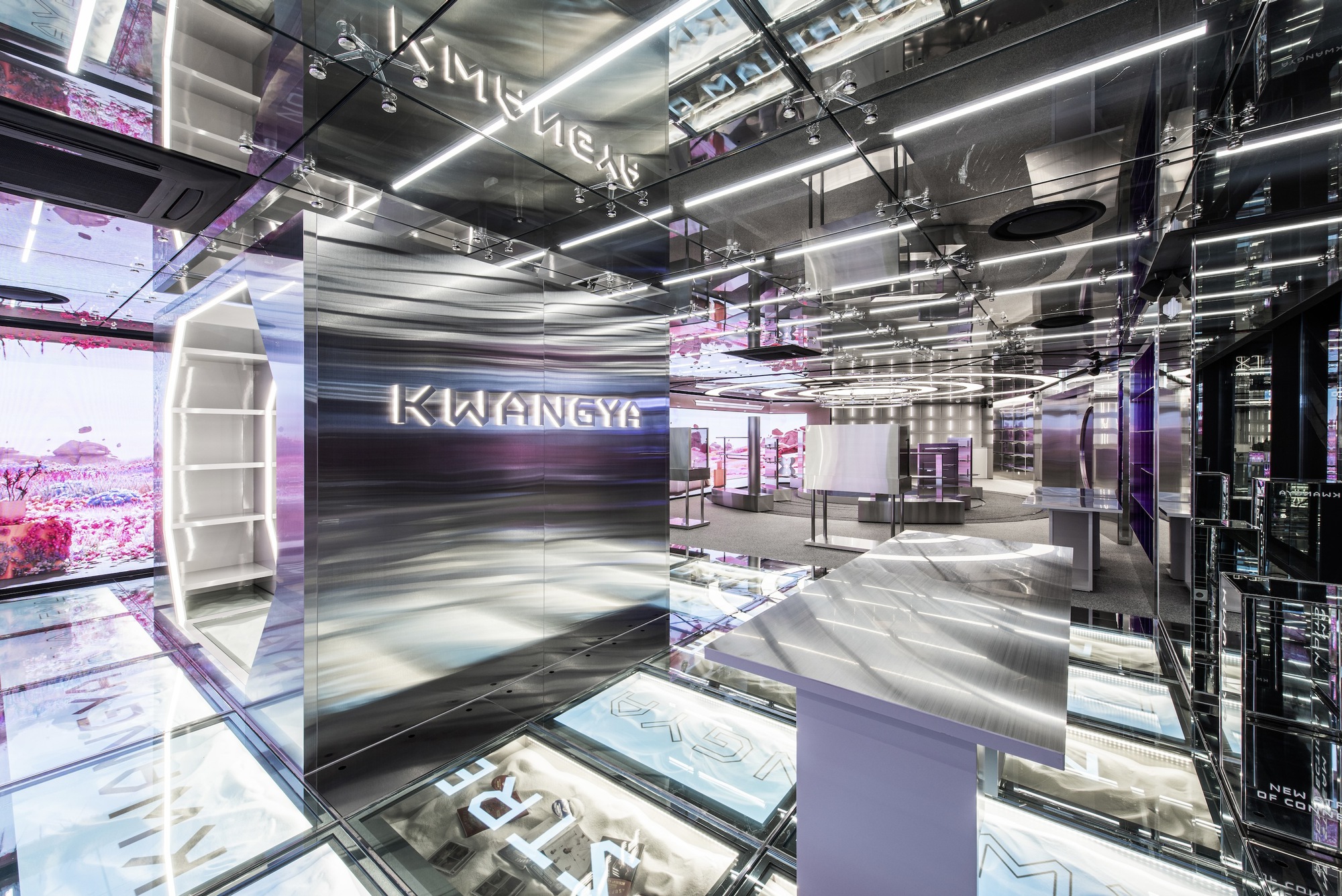 Polished stainless steel reception desk beneath reflective ceiling panels and linear lighting strips