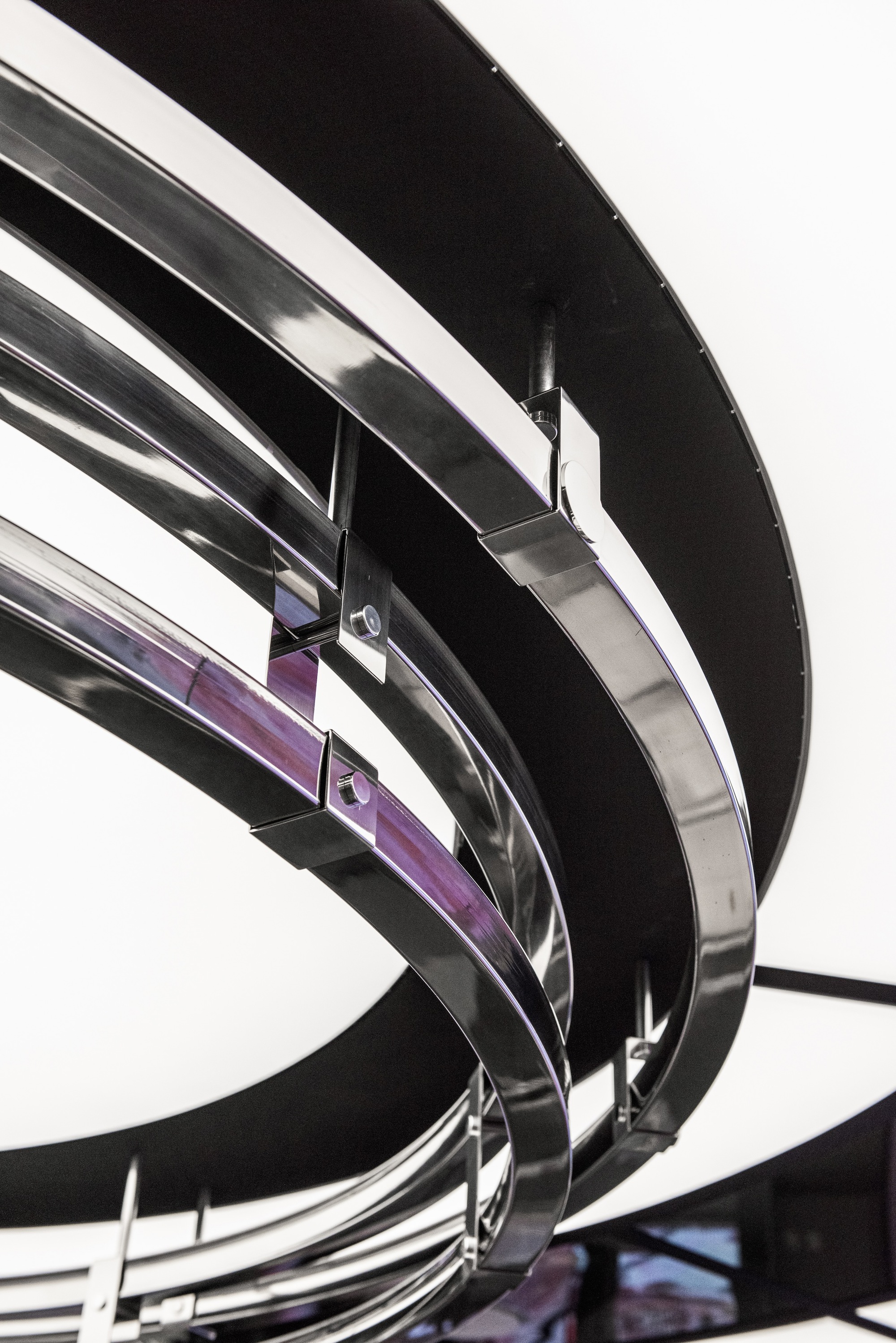 Close-up of curved black metal banding wrapping around purple glass panels in an interior stairwell