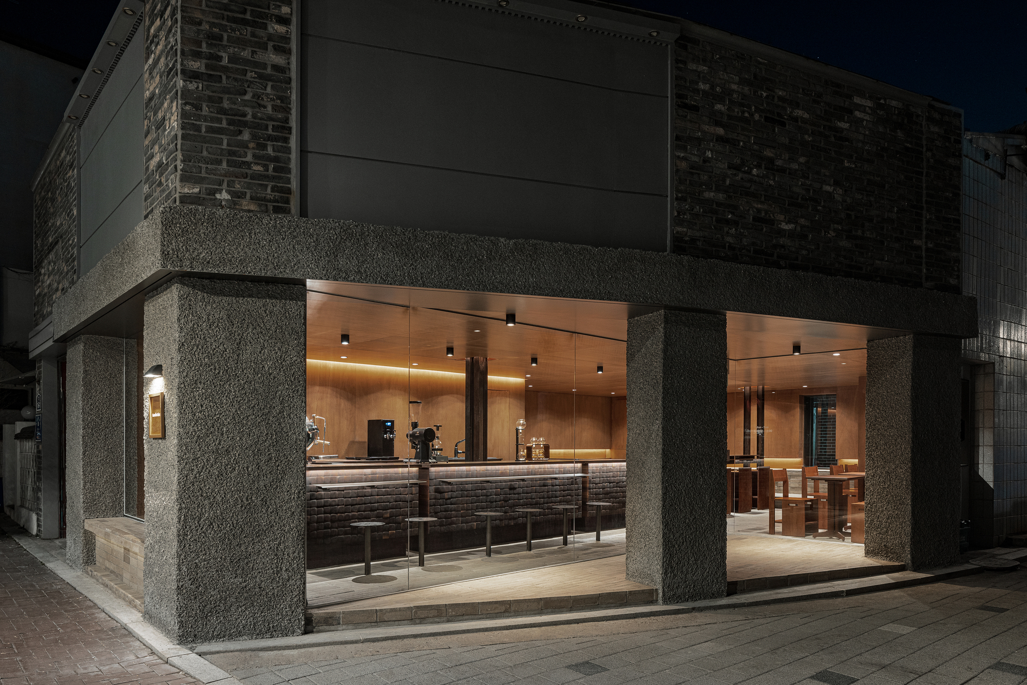 Street corner view of the open glass facade with textured concrete columns at night