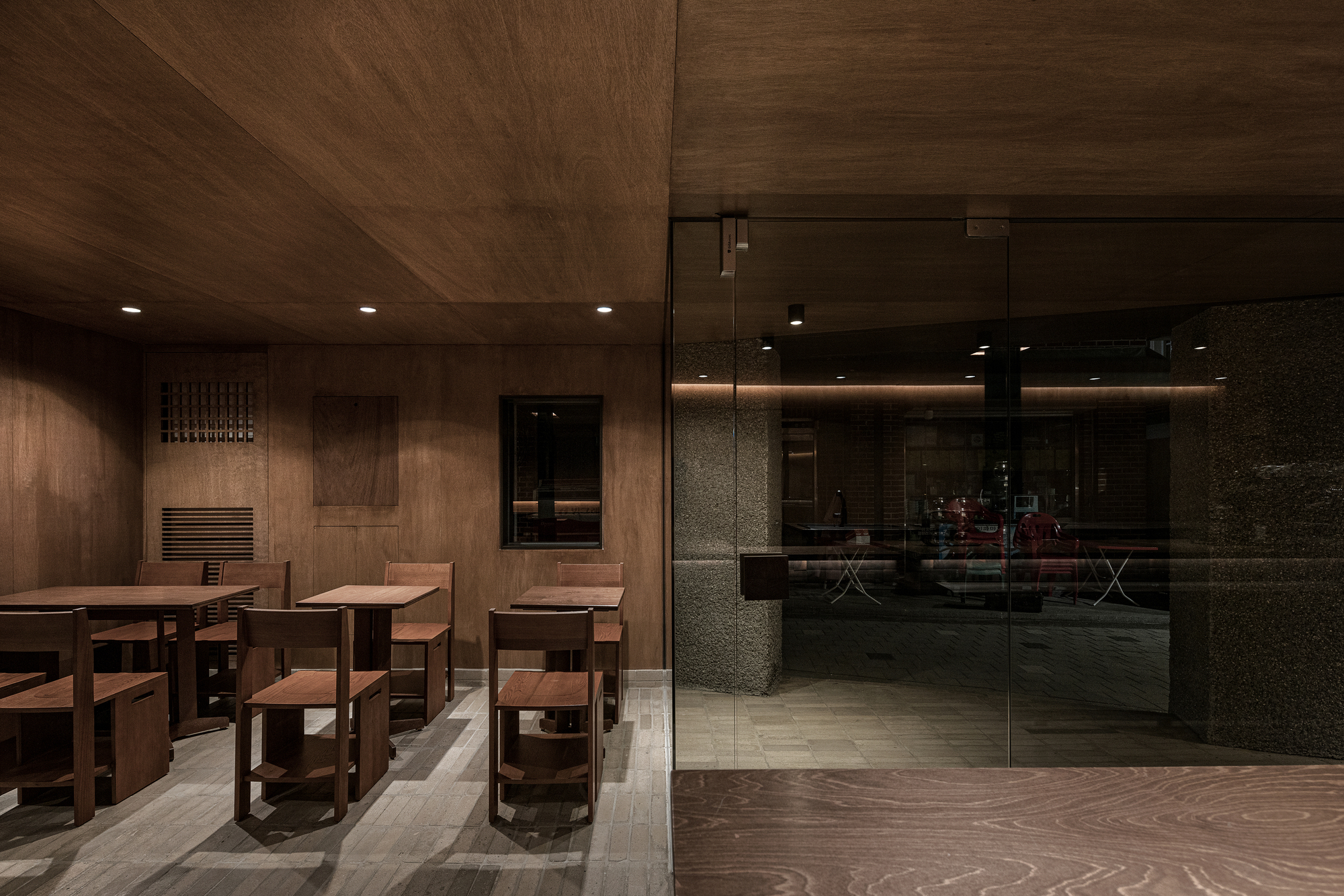 Seating area with wooden tables and glass partition separating dining from service counter