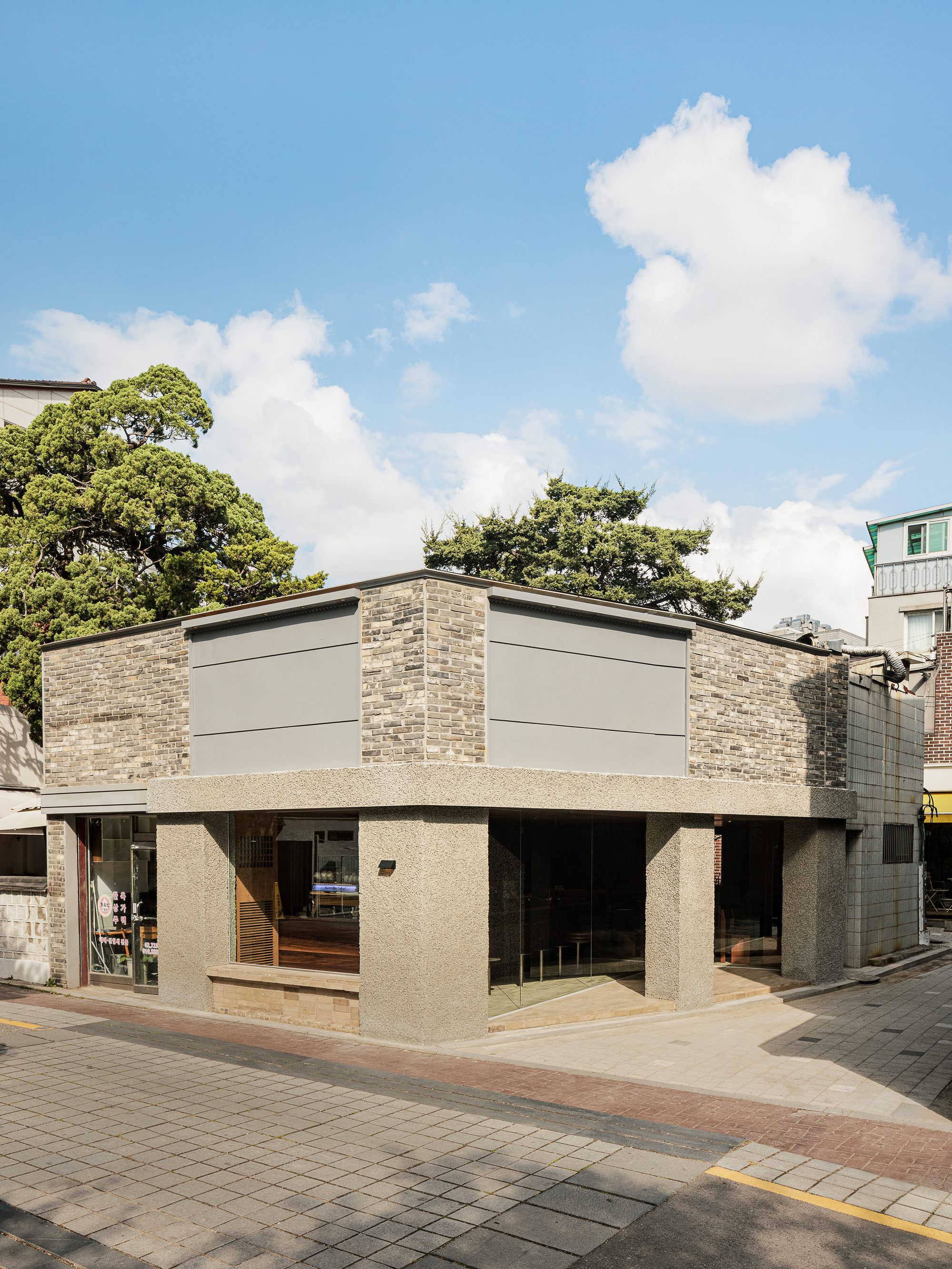 Corner elevation showing brick and panel facade with exposed aggregate concrete base under clouds