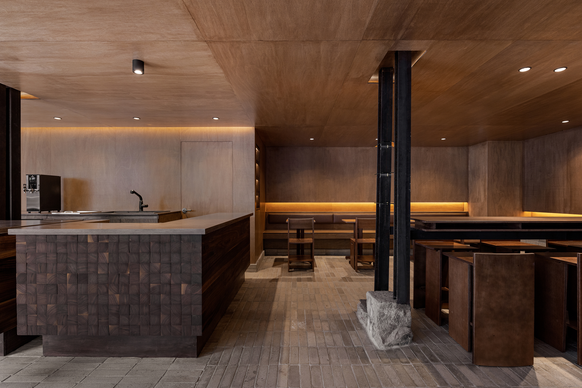 Interior of a tea room with textured wood ceiling, stone counter, and black steel columns with carved stone bases