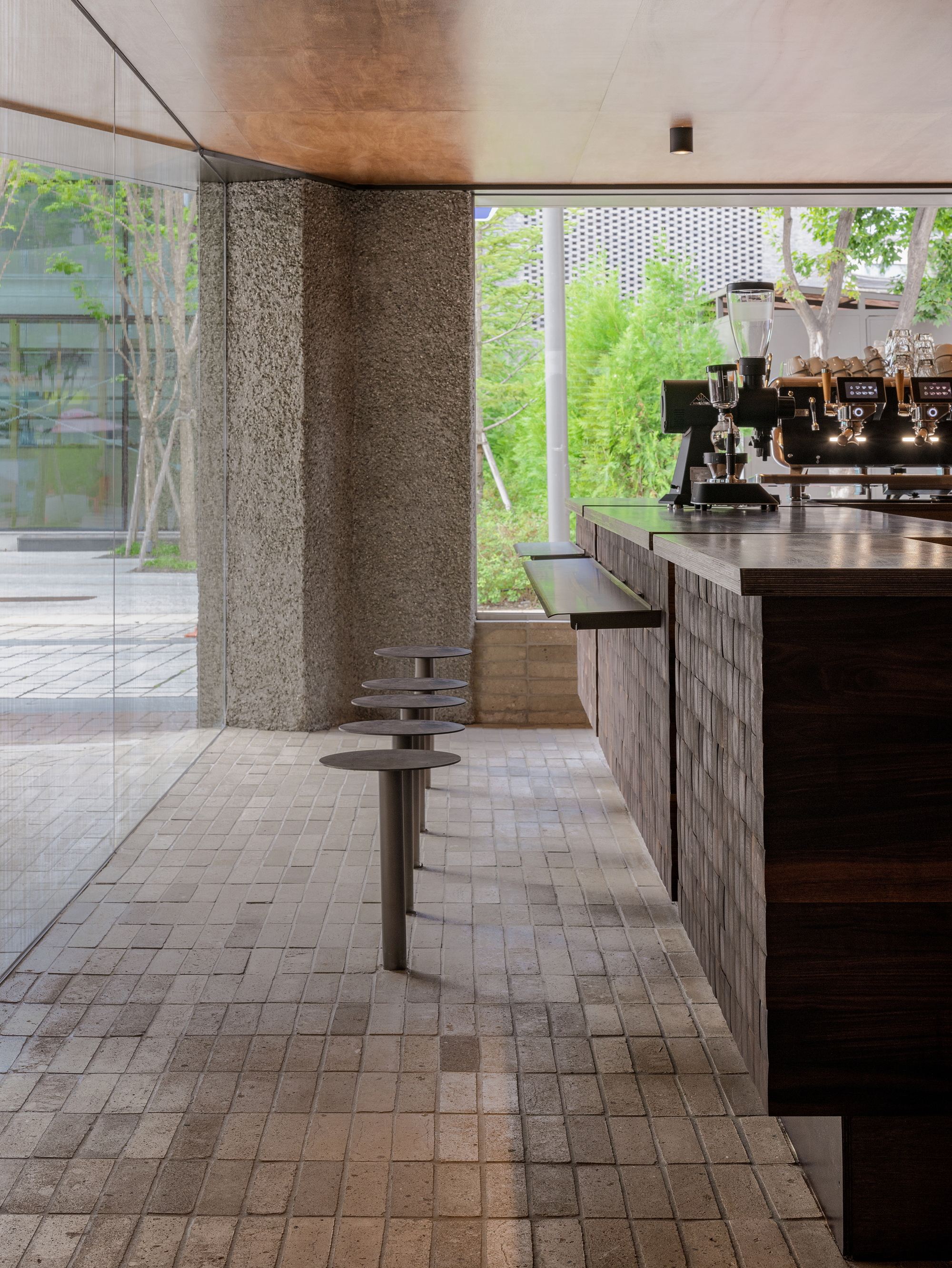 Rough stone wall beside a counter with circular metal stools overlooking a planted courtyard through large windows