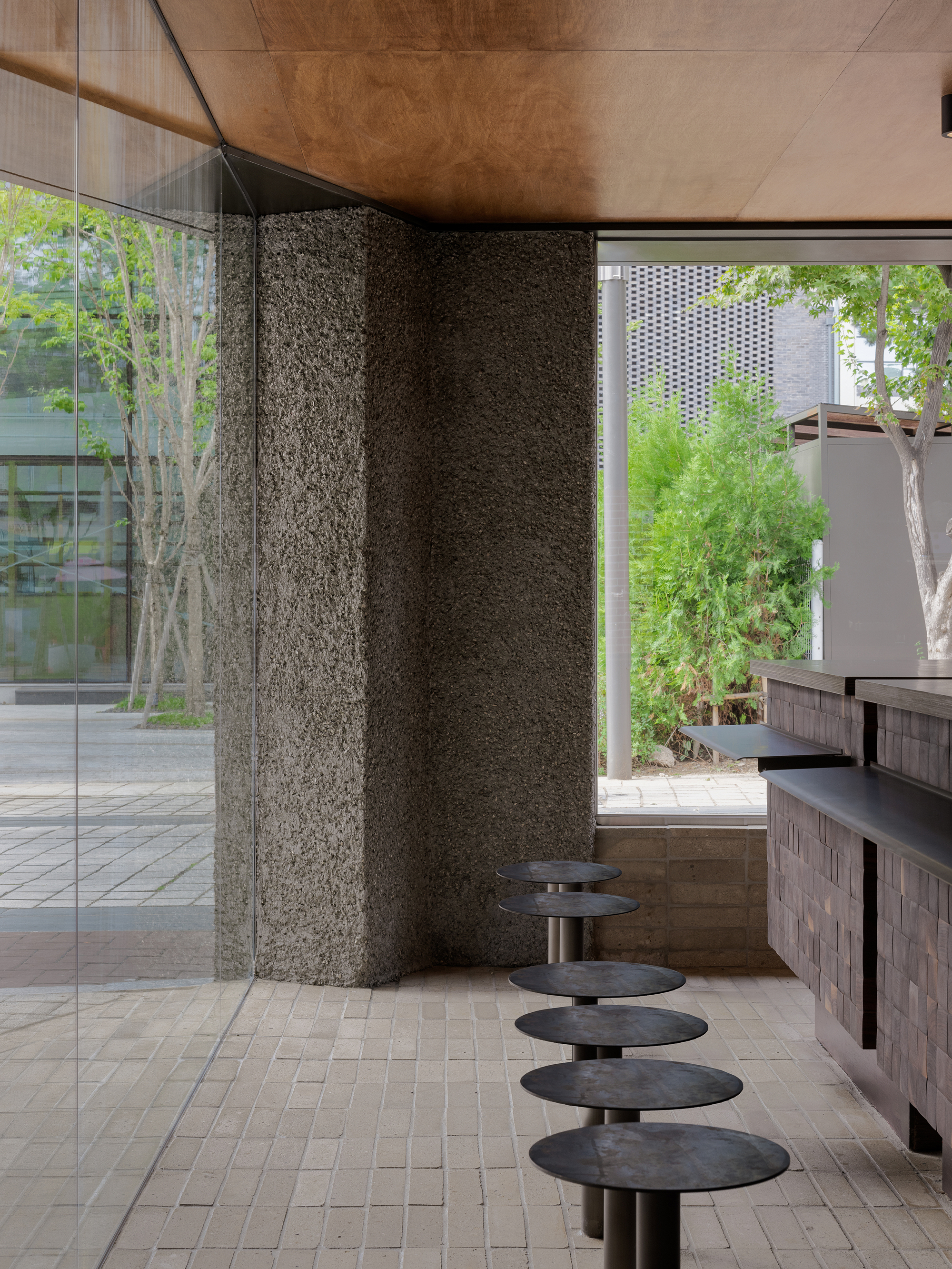 Row of round metal stools extending along the counter toward a glazed opening with trees visible outside
