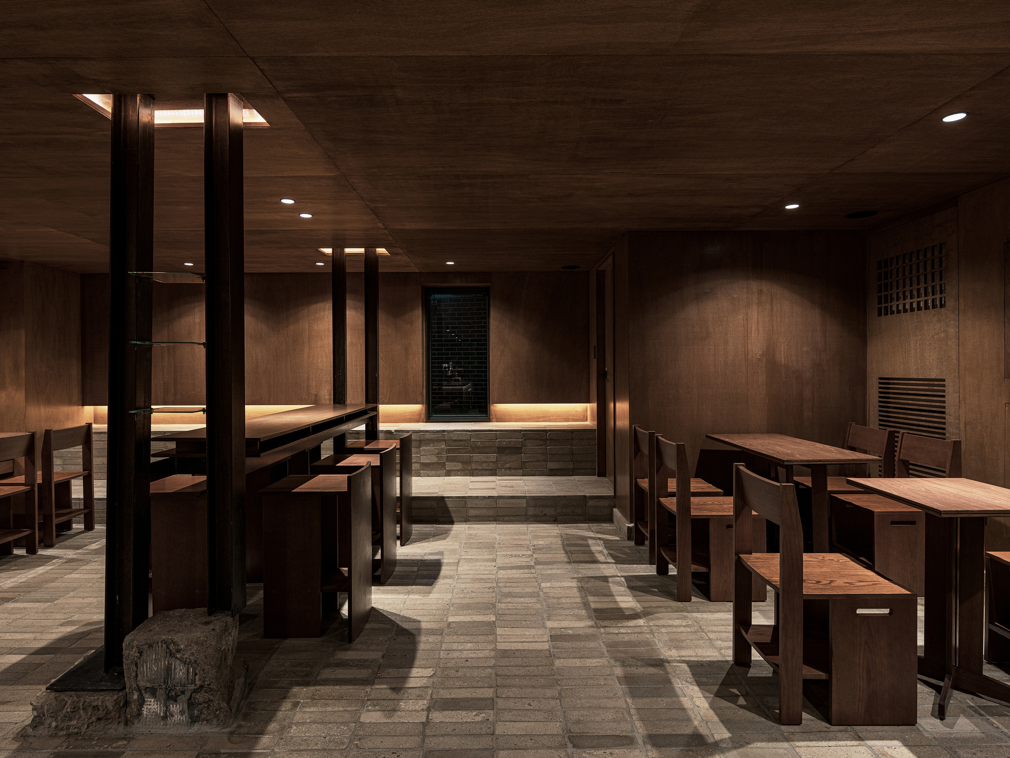 Interior dining area with timber benches and tables arranged beneath a wood ceiling with recessed lighting