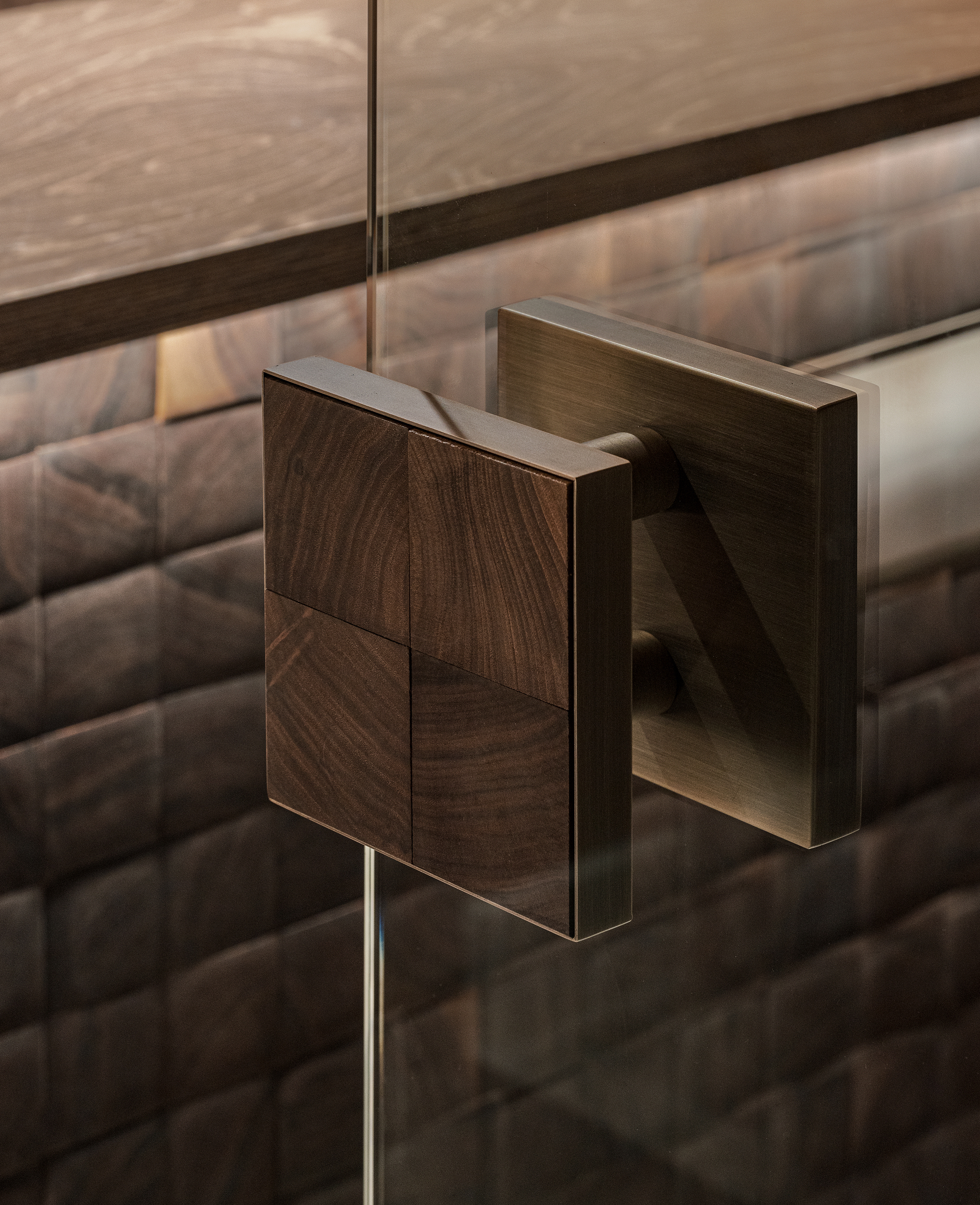 Close-up of a brushed metal door handle with walnut veneer plate against textured tile wall